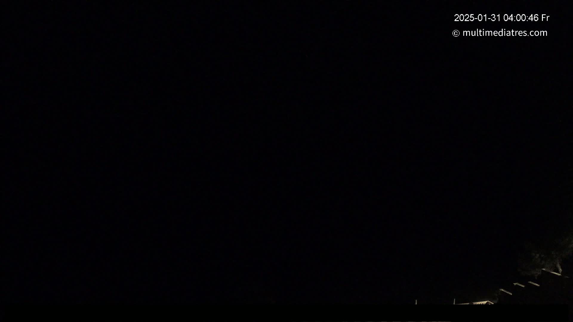 A dark nighttime scene shows a few dimly lit structures at the bottom edge of the frame against a completely black sky.