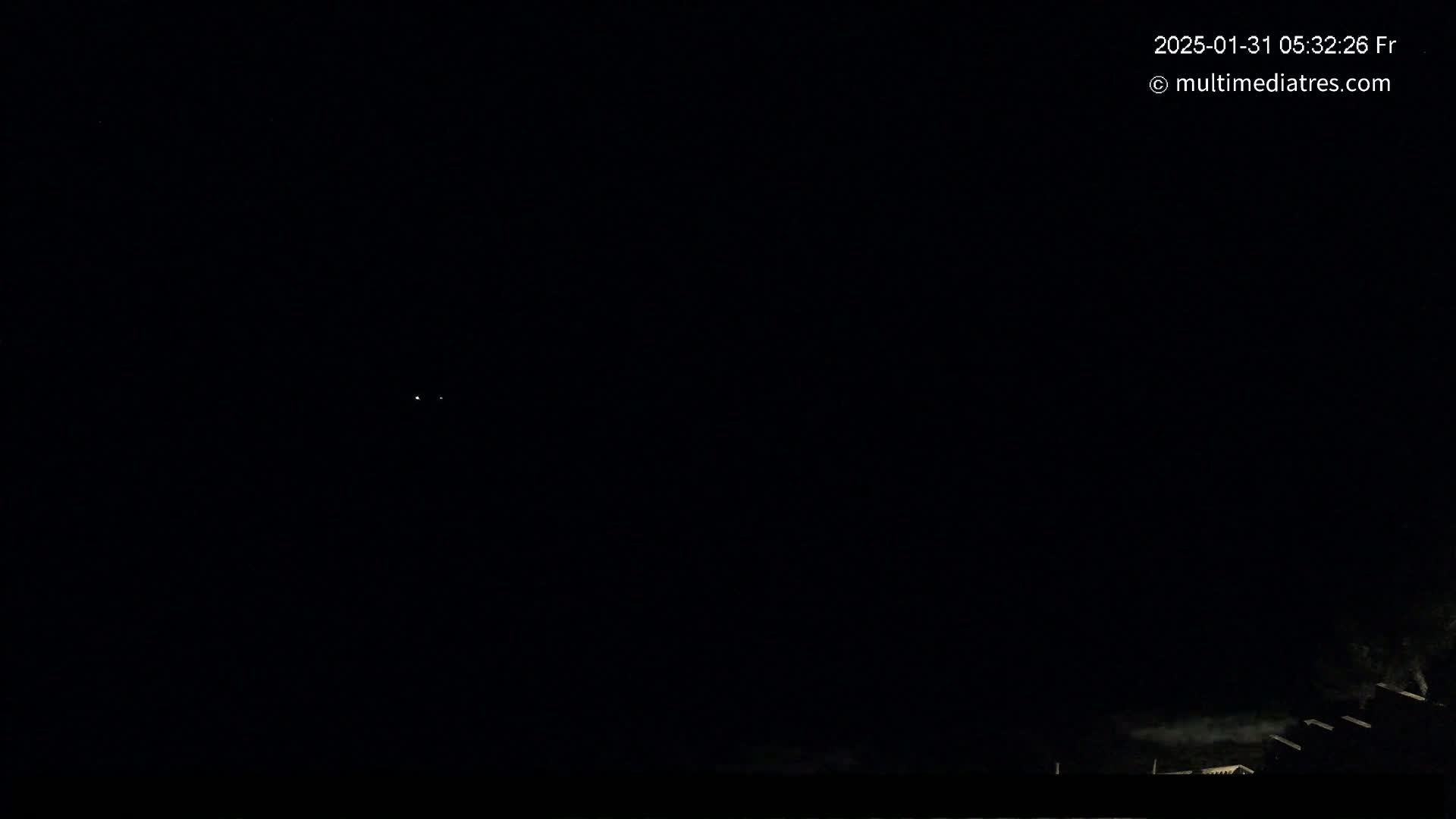 A nighttime scene shows a dark sky with a few faint lights in the distance and the silhouettes of buildings or trees at the bottom.