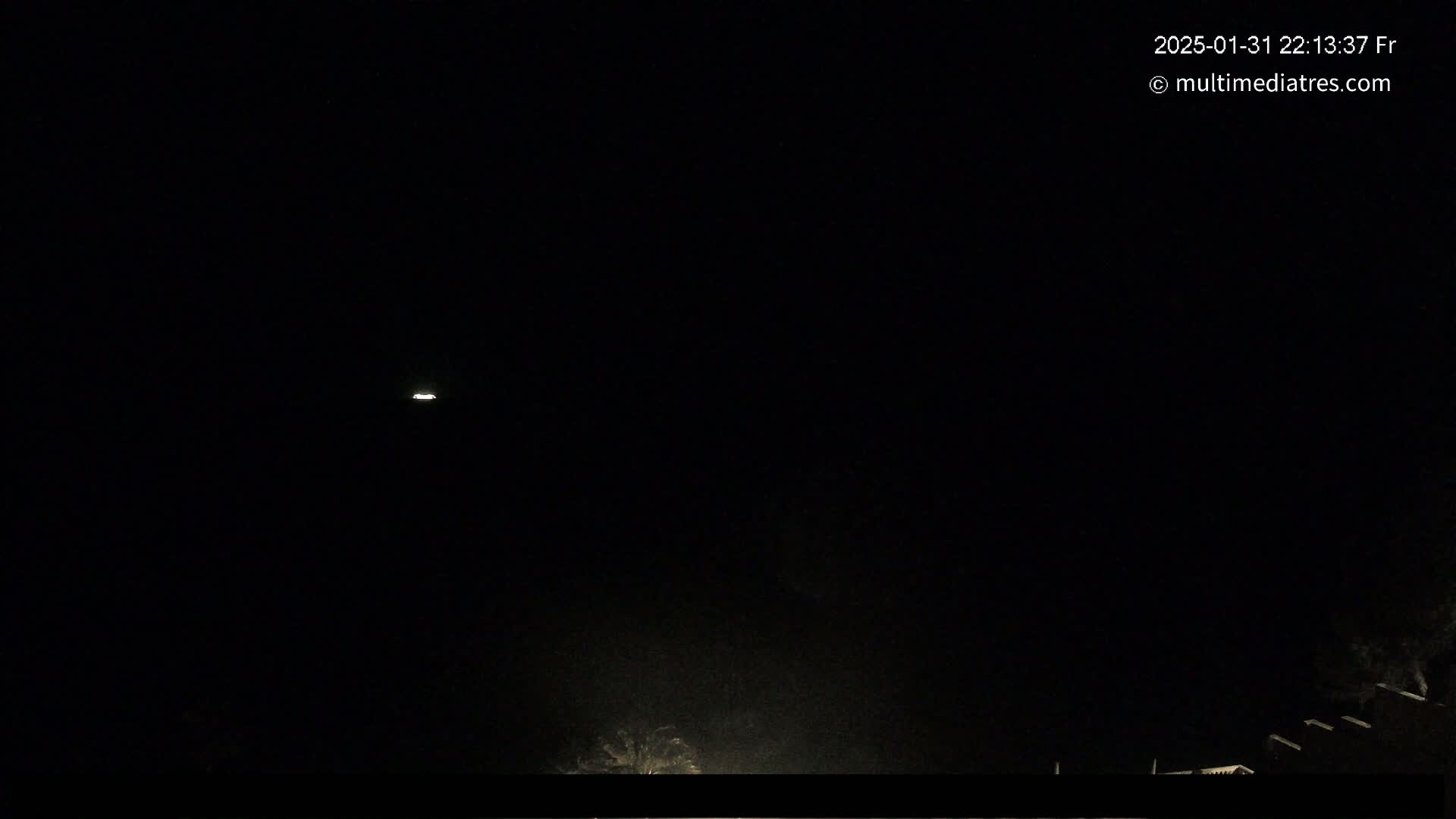 A dark nighttime scene shows a faint light in the distance and dimly lit structures at the bottom of the frame.