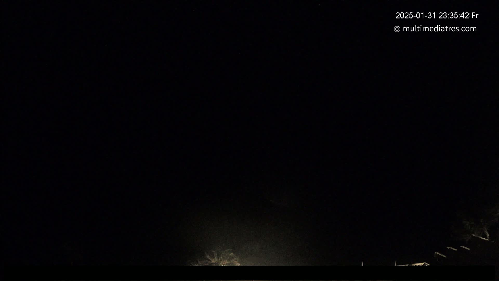 A dark nighttime scene shows a dimly lit area with some structures at the bottom of the frame under a clear, black sky.