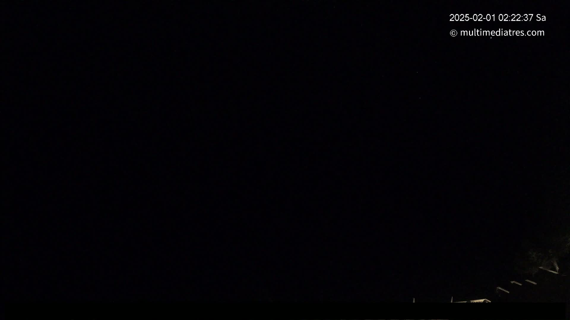 A mostly dark nighttime scene shows a sliver of faintly lit buildings at the bottom of the frame under a clear, starlit sky.