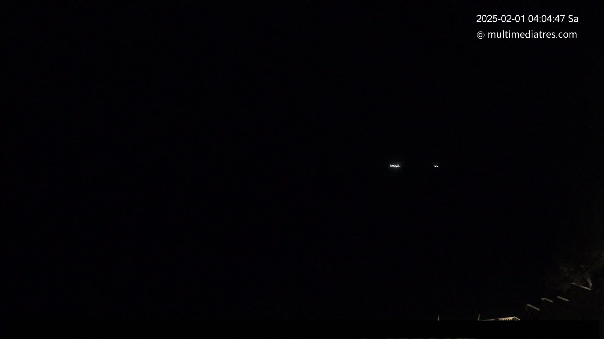 At night, two distant lights are visible in a dark sky above a low-lying, dark structure.