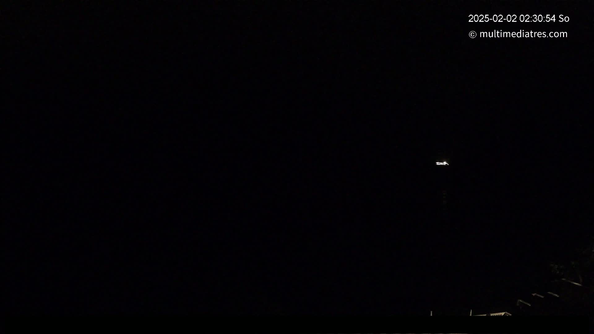 A distant light is visible in a dark, nighttime sky above a low-lying, dark silhouette of structures.
