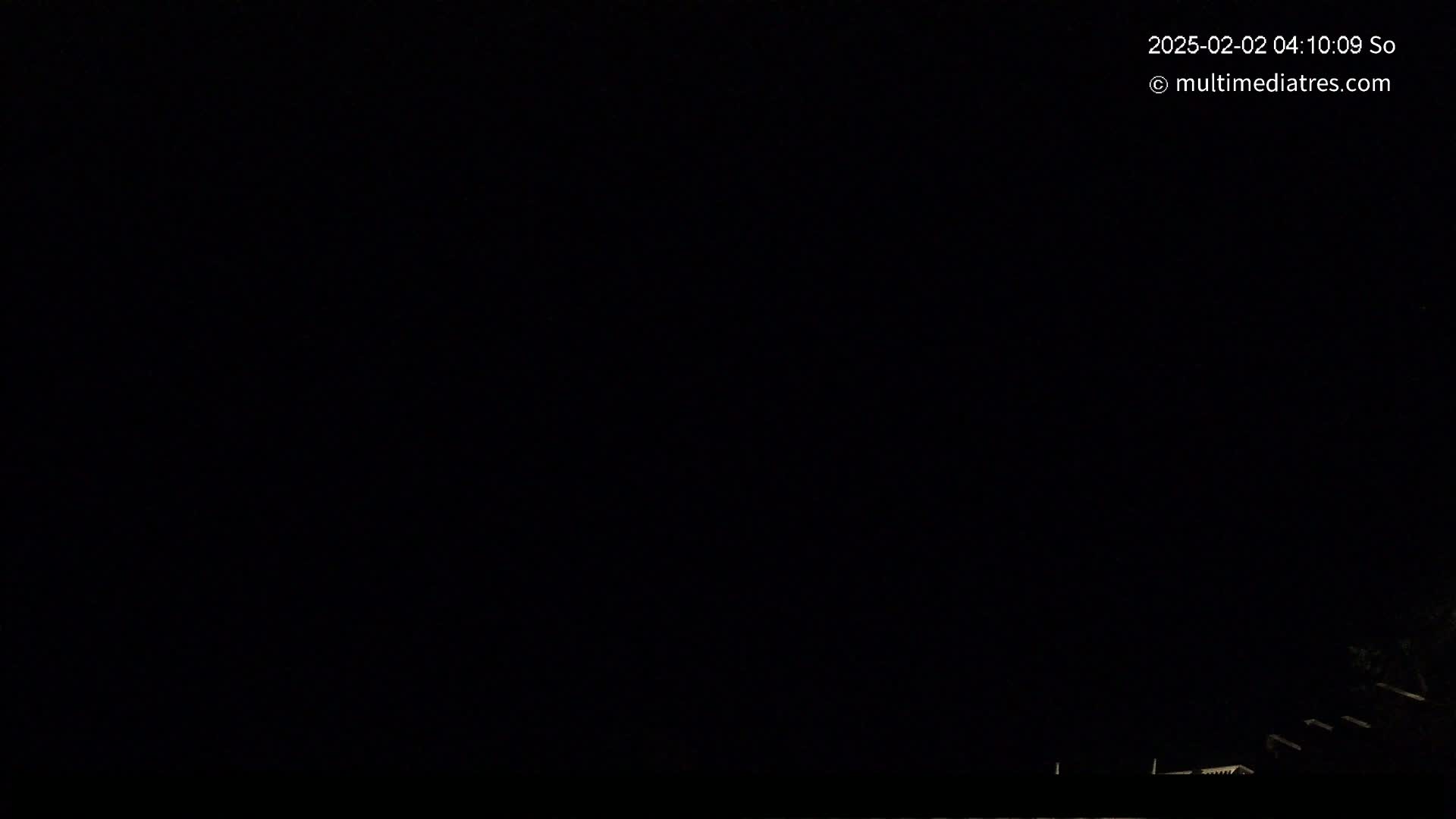 A very dark, nighttime scene shows a few dimly lit rooftops at the bottom edge of the frame.