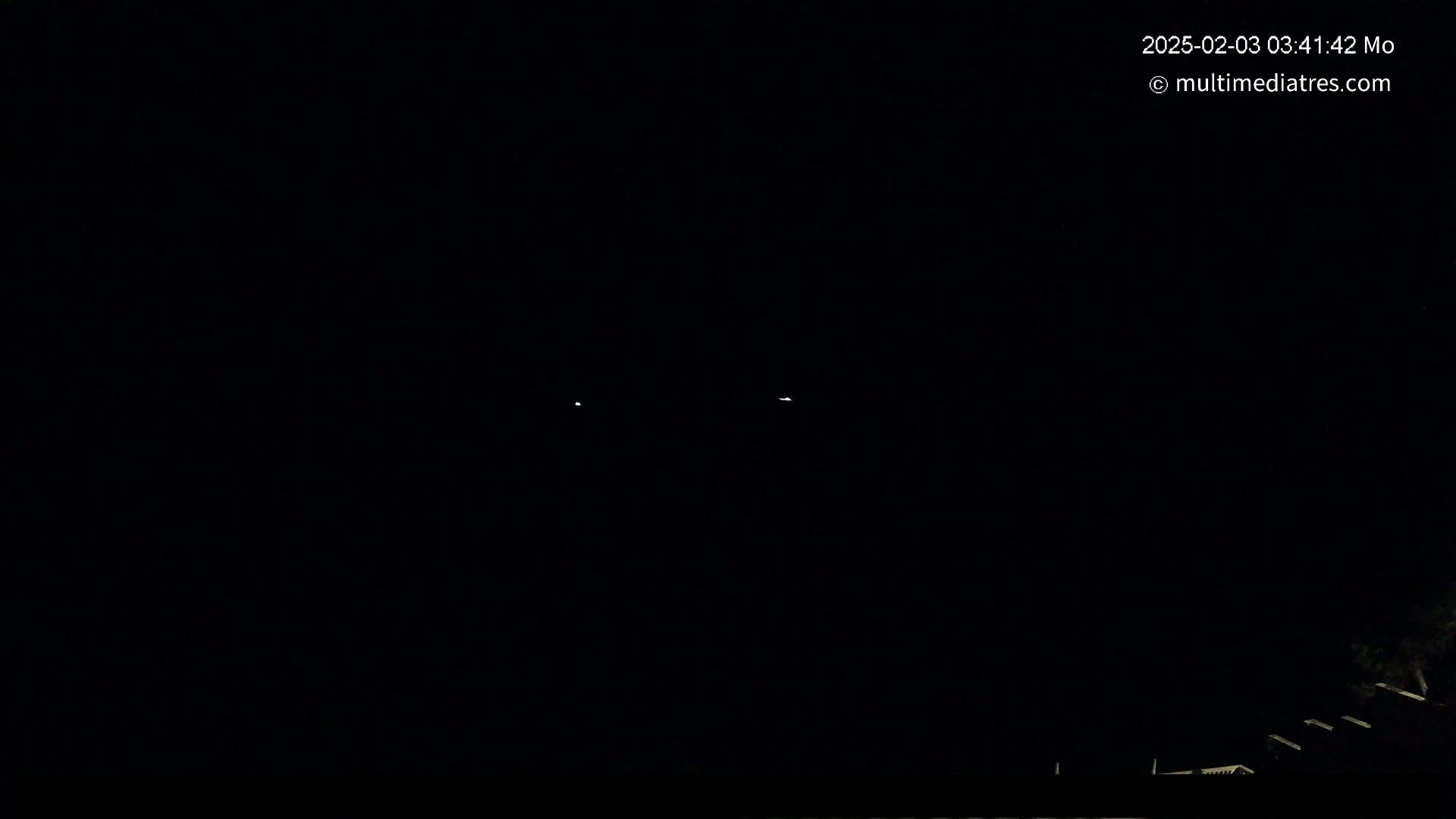 The image shows a nighttime outdoor scene with two faint lights in the distance and a dark, possibly silhouetted structure at the bottom.