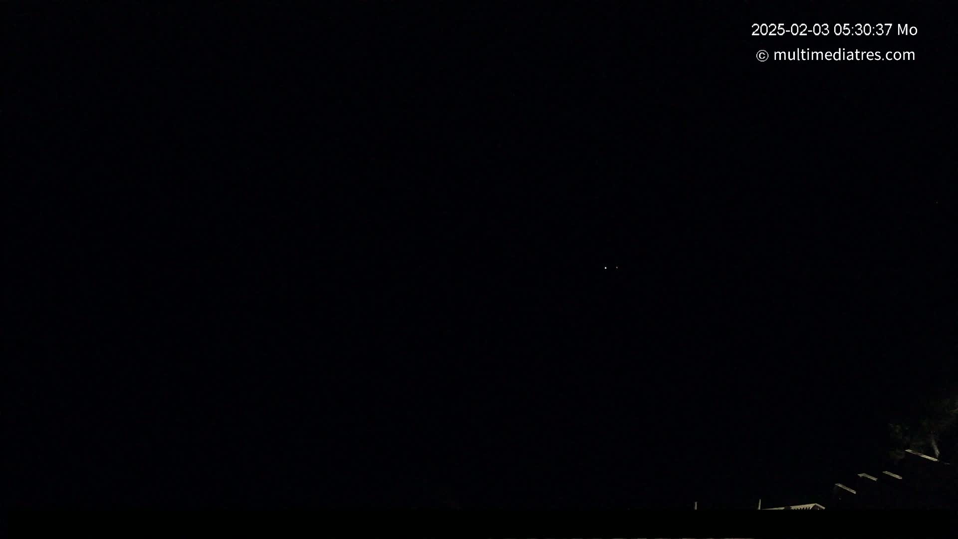 A nighttime outdoor scene shows a dark sky with a few faint lights visible in the distance, and a dark silhouette of structures at the bottom of the frame.