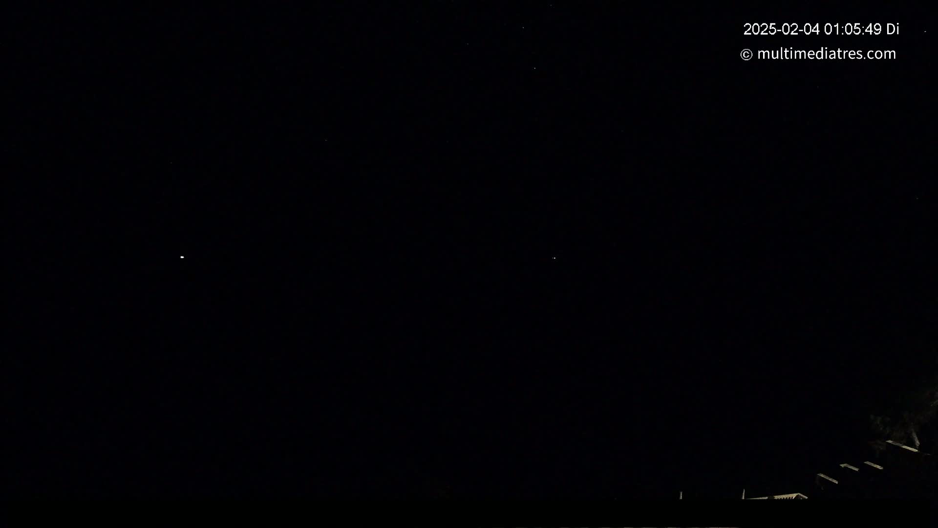 A nighttime outdoor scene shows a dark sky with a few faint stars and the silhouettes of structures at the bottom.