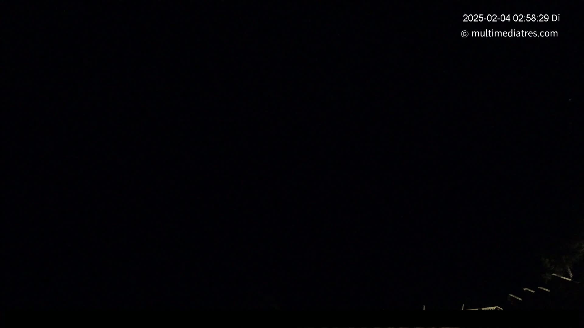 The image shows a dark nighttime scene with a few dimly lit structures visible at the bottom.