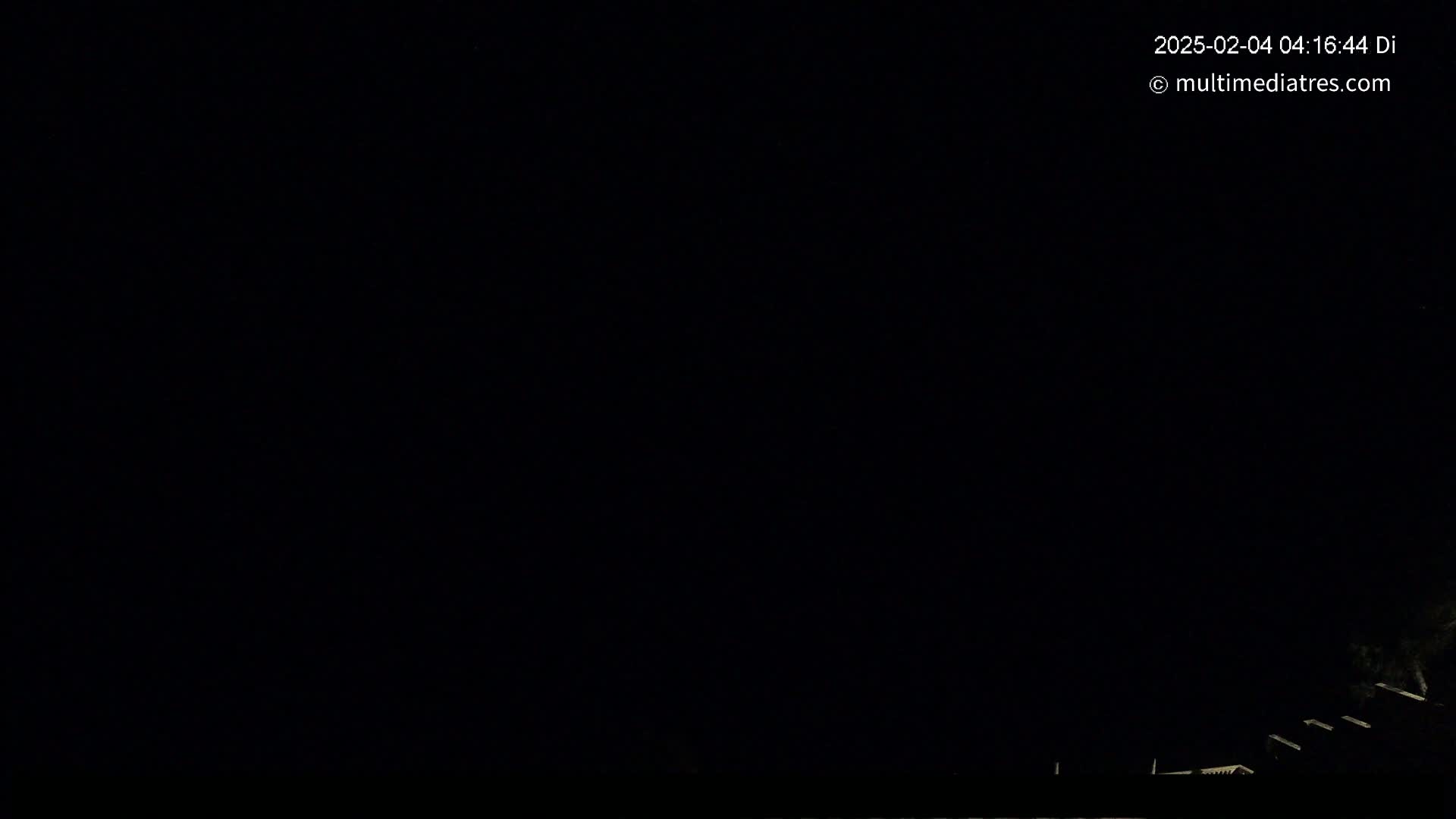 A dark, nighttime scene shows the silhouettes of structures at the bottom edge of the frame against a completely black sky.