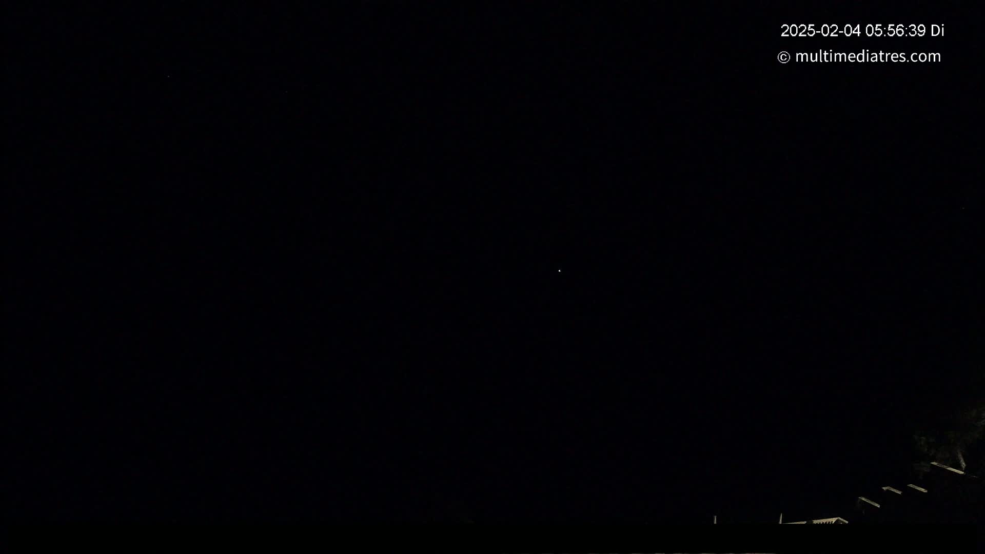 A dark night sky with a single, faint light visible, and a dark silhouette of structures and some vegetation at the bottom.