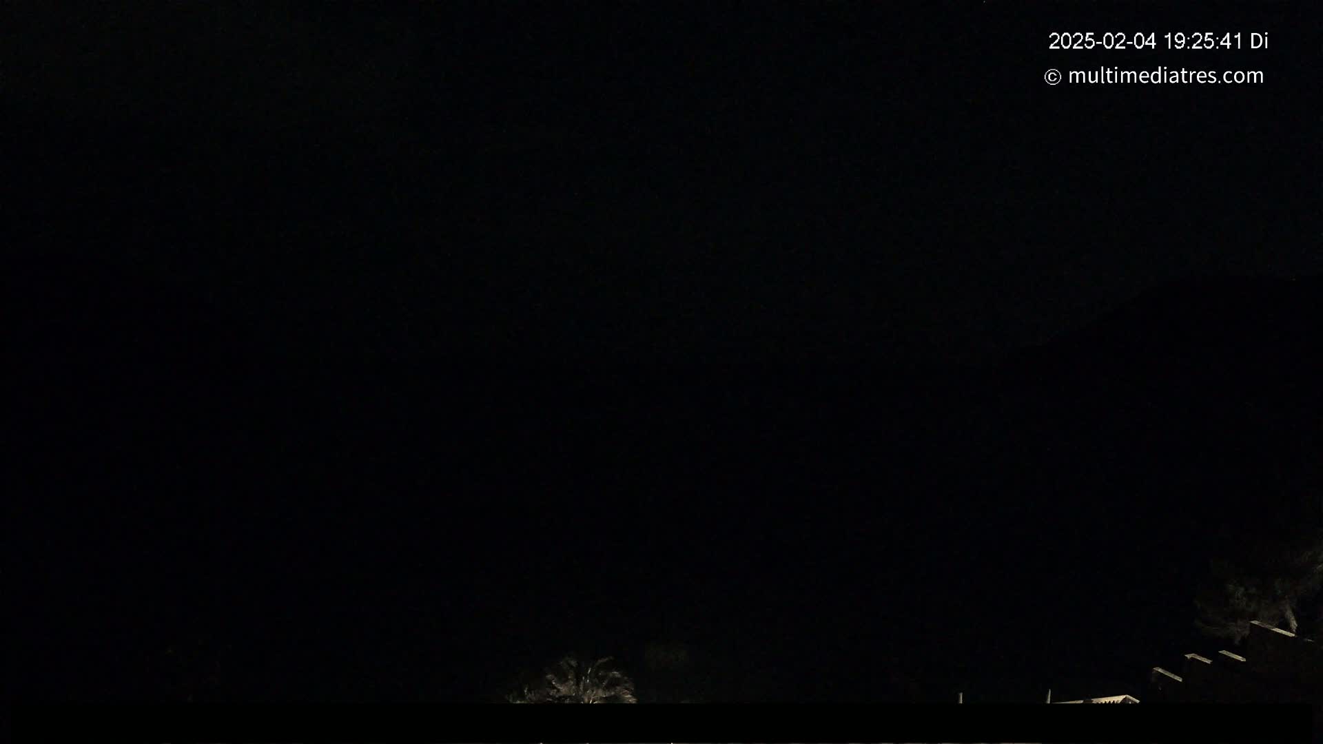 The image shows a dark nighttime scene with a few dimly lit structures and vegetation visible at the bottom.