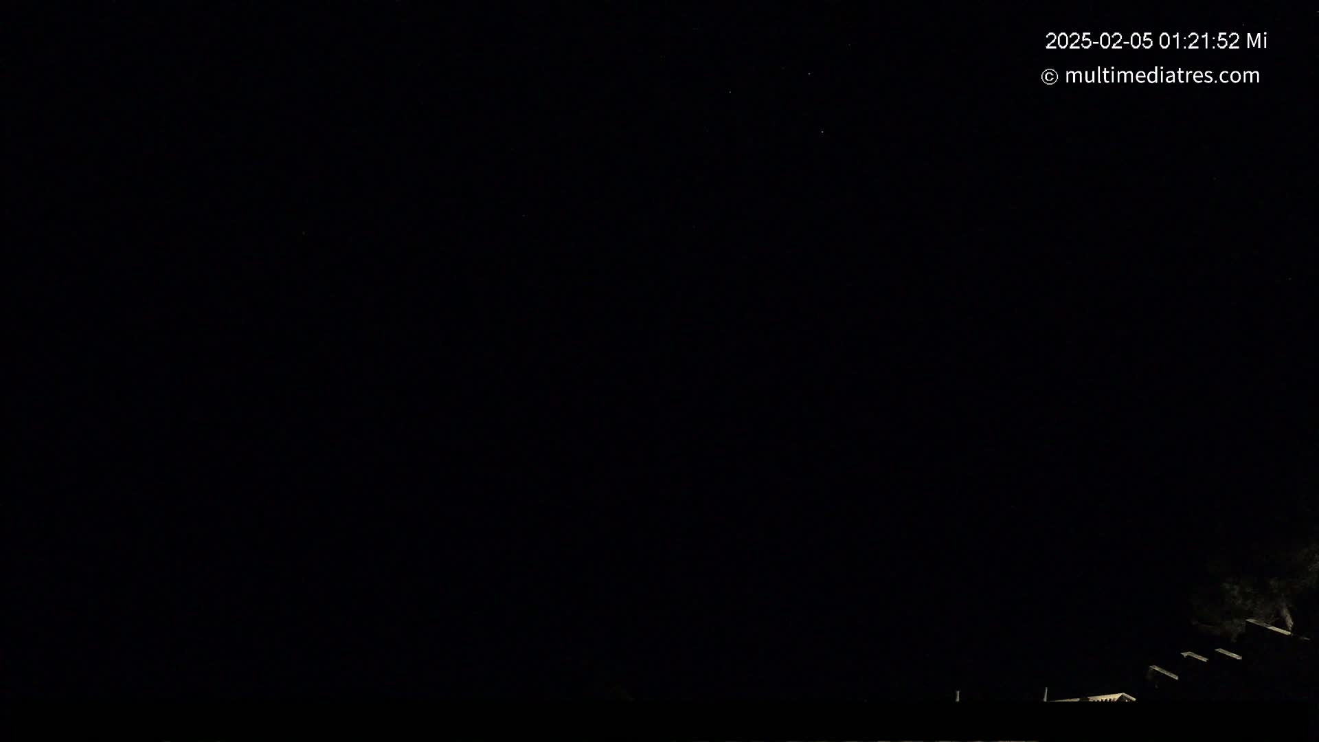 A nighttime image shows a mostly clear, dark sky with a few faint stars and dimly lit structures at the bottom.
