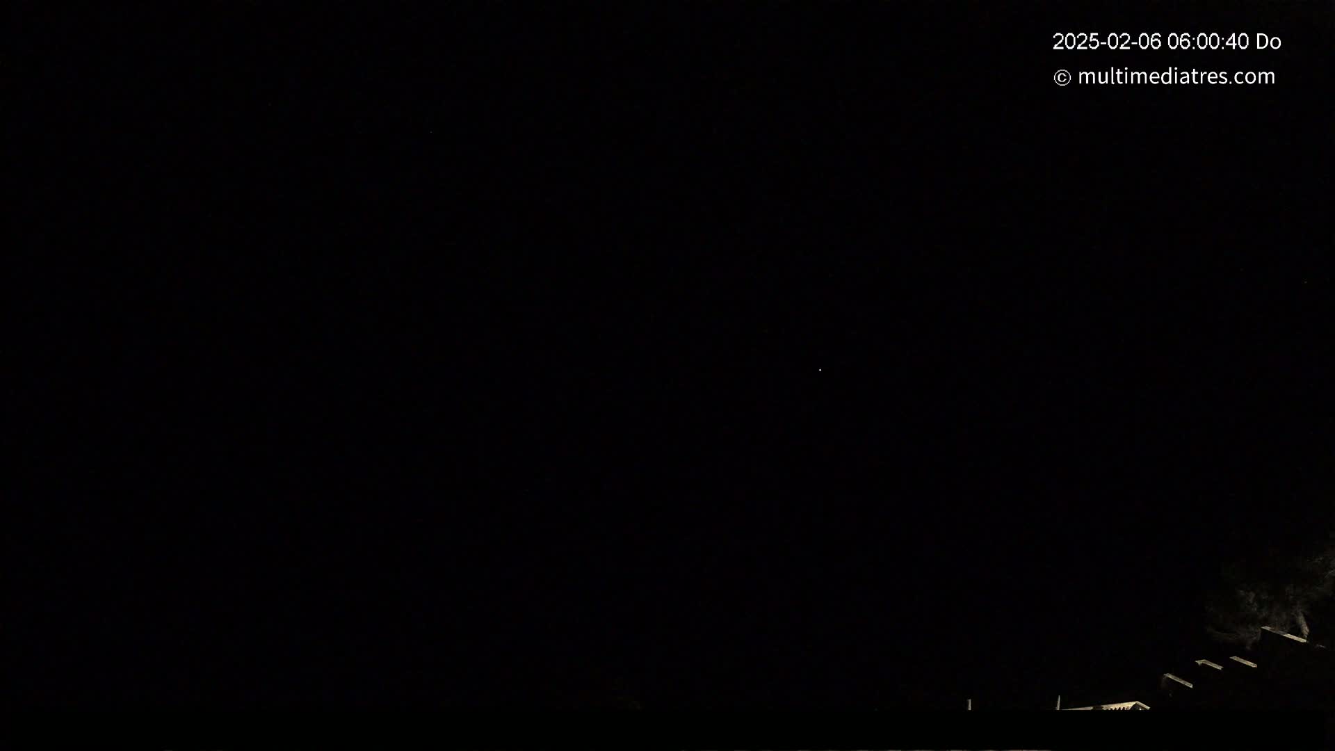 A dark night scene shows a very faint light in the sky above a low, dark structure.