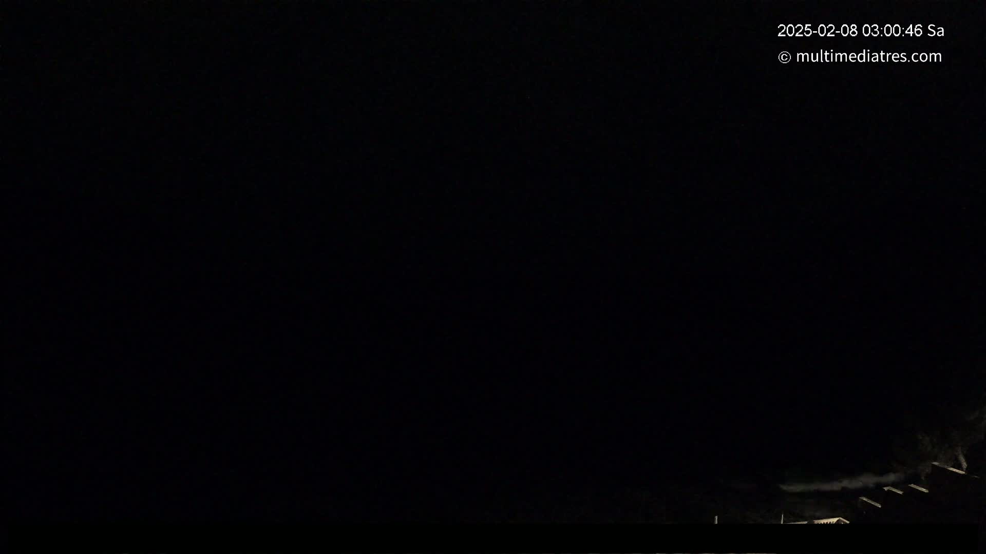 A nighttime, low-light outdoor image shows the tops of dark buildings faintly visible against a completely black sky.