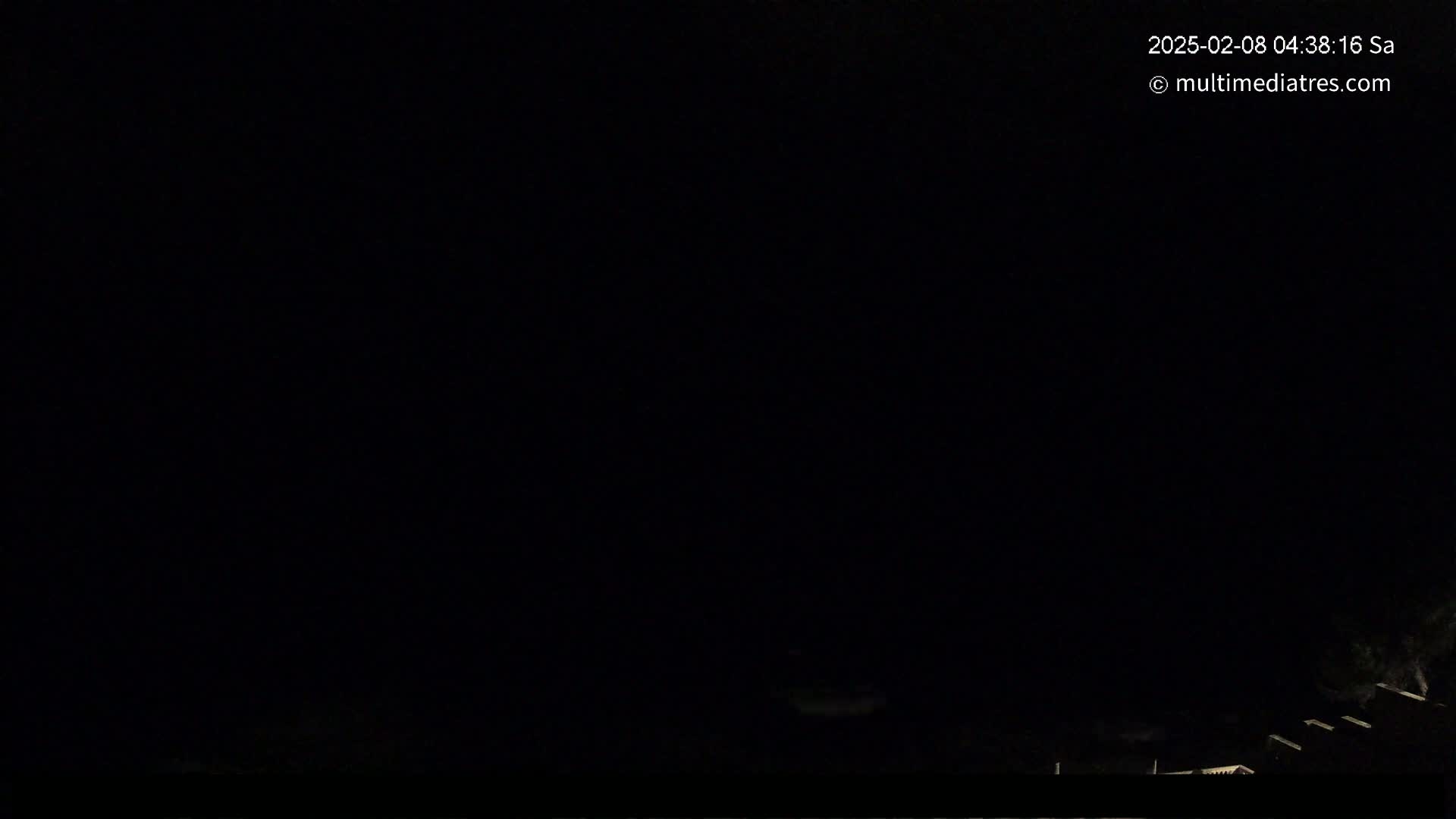 A nighttime, dark outdoor scene shows a few dimly lit structures at the bottom of the frame against a completely black sky.