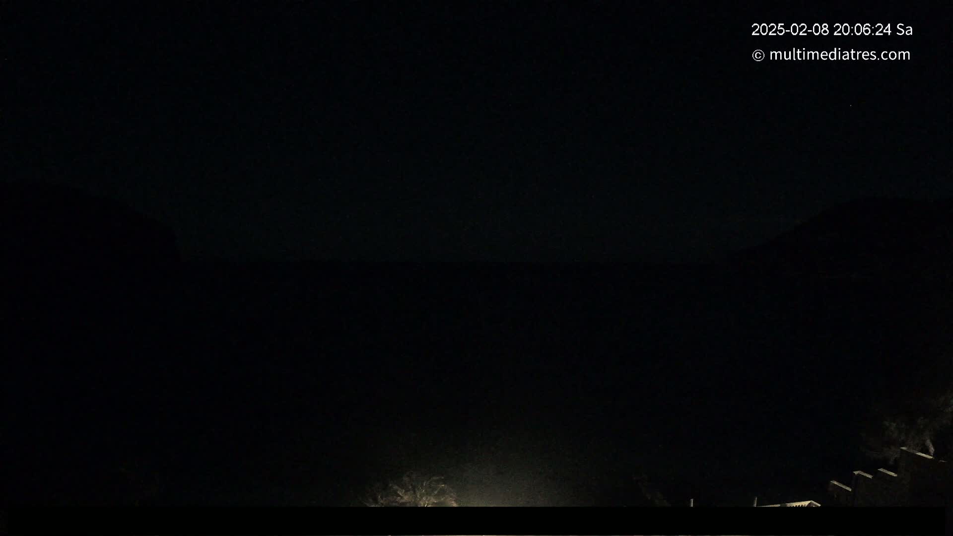 A nighttime, dark view shows a mostly black scene with some dimly lit vegetation at the bottom.