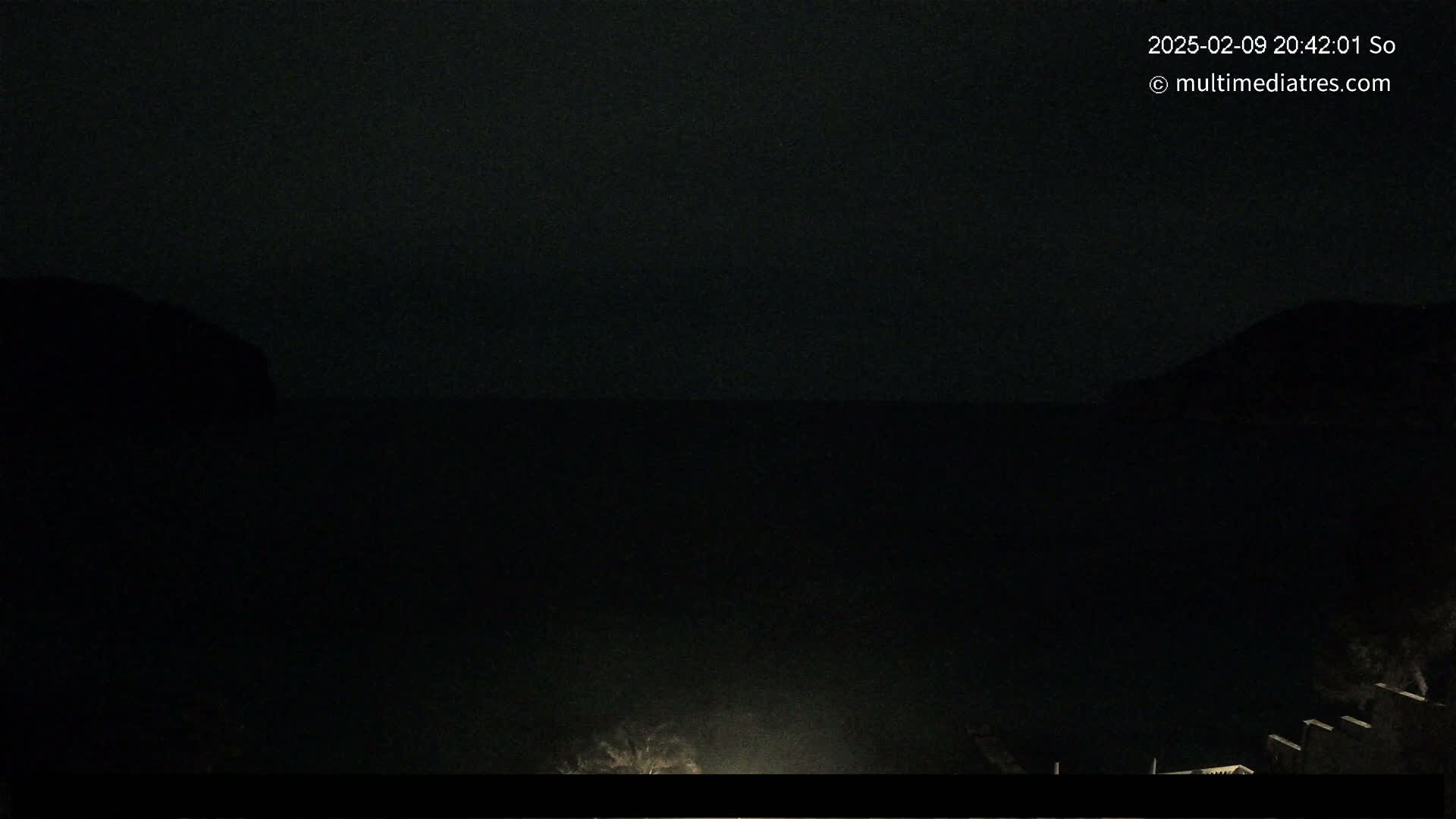 A dark, nighttime view of a body of water between two silhouetted hills.