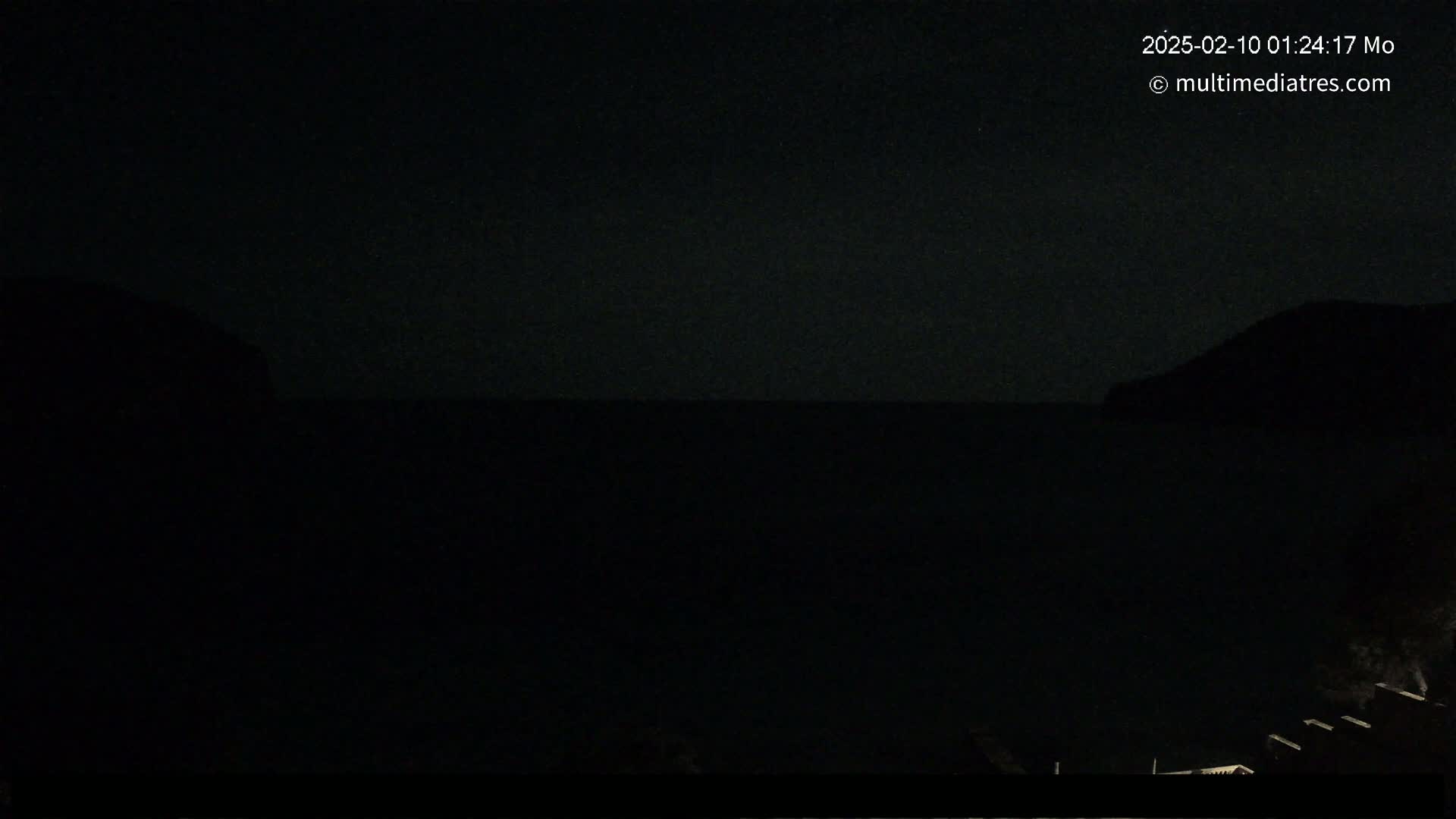 A nighttime view of dark water between two silhouetted landmasses under a clear, starry sky.