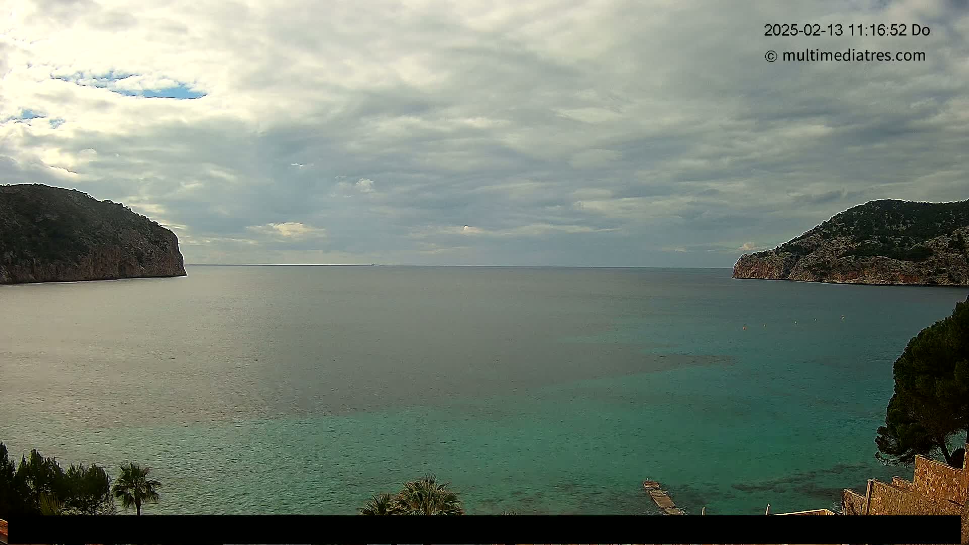 A partly cloudy day shows a tranquil teal bay nestled between two rocky hillsides.