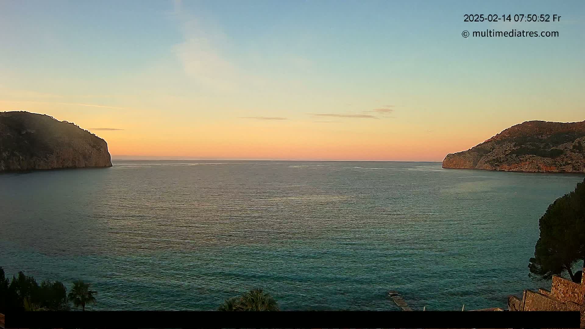 A calm sea at sunset is nestled between two rocky headlands.