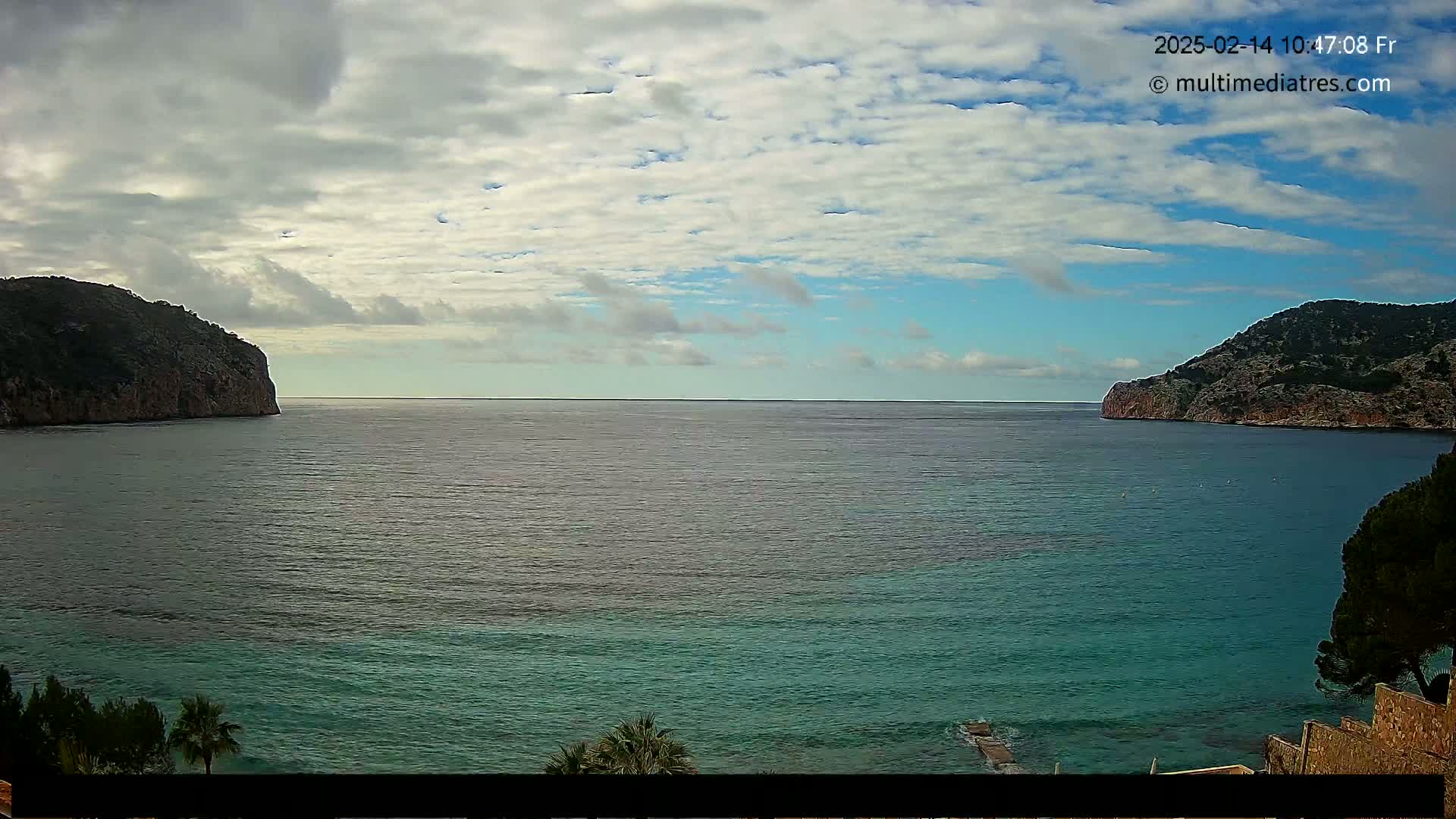 A partly cloudy day shows a tranquil ocean scene, with two rocky headlands framing a calm bay.