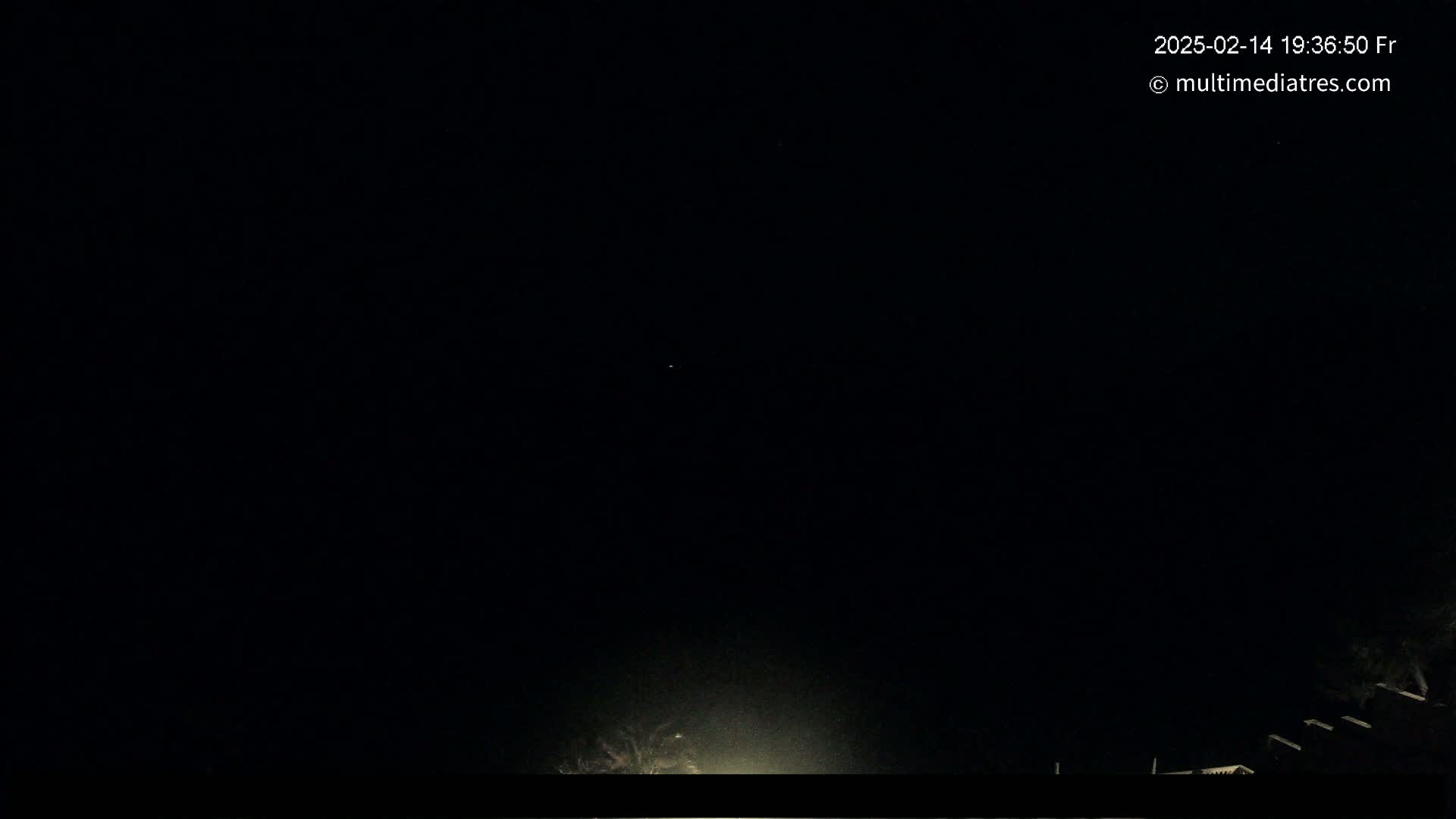 A nearly pitch-black nighttime scene shows a few faint lights at the bottom of the frame against a dark sky.
