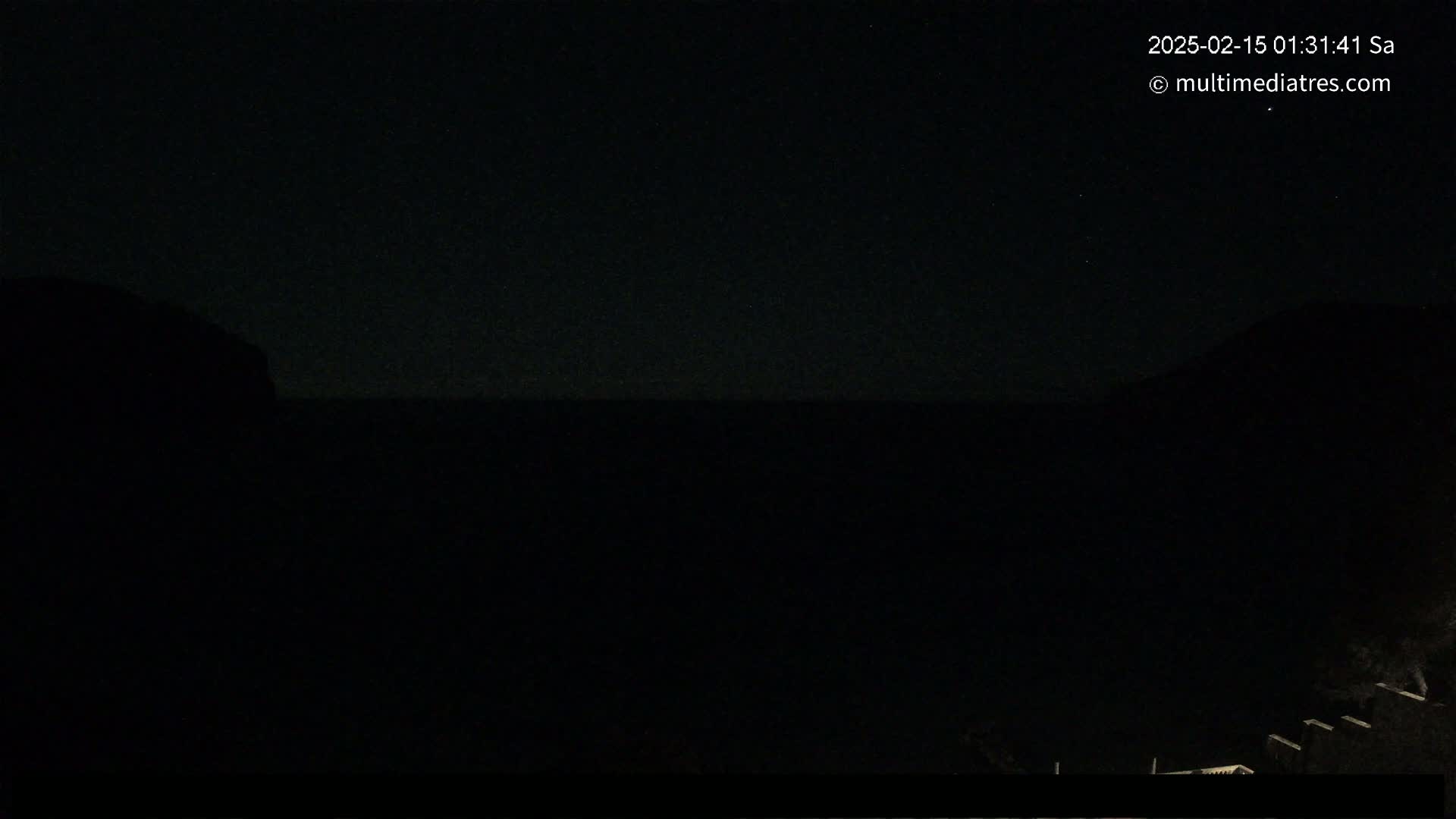 A nighttime, dark view of a body of water between two darkened hills under a starlit sky.