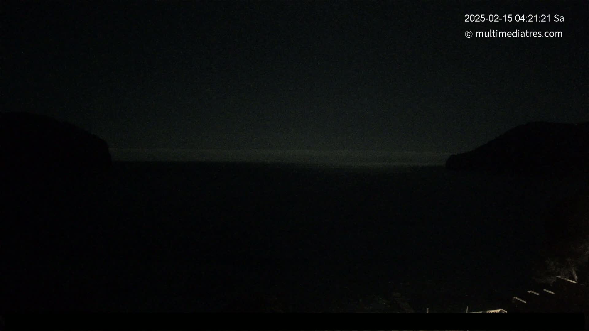 A dark nighttime view shows a body of water between two silhouetted landmasses.