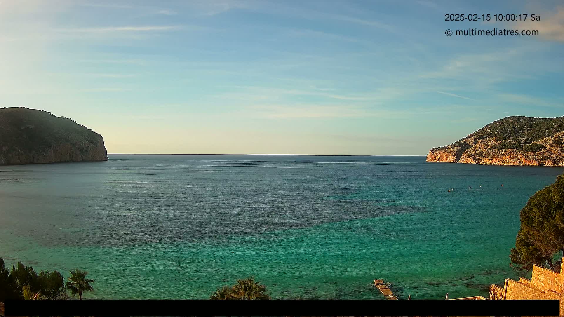 A calm, clear day reveals a turquoise bay nestled between two verdant hillsides.