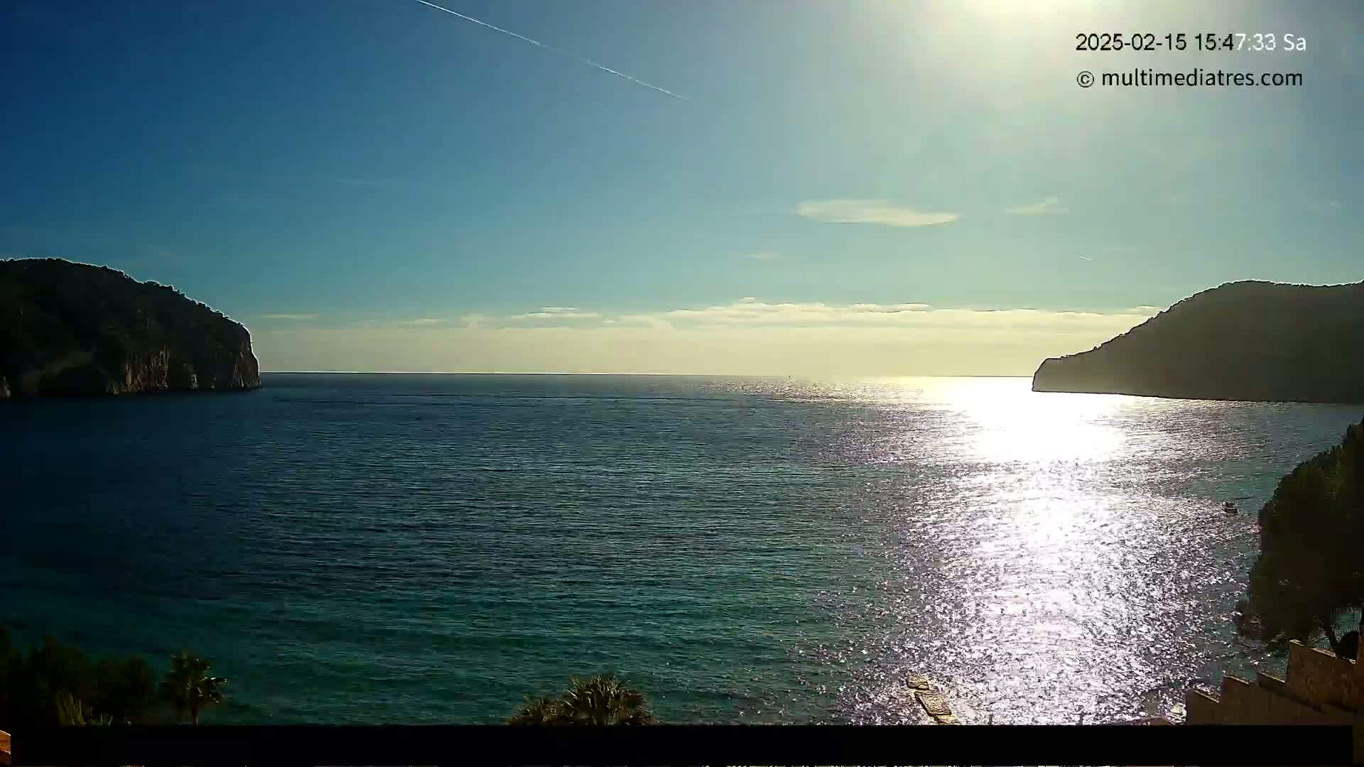 A calm, sunny day reveals a sparkling expanse of sea nestled between two dark, rocky hills.