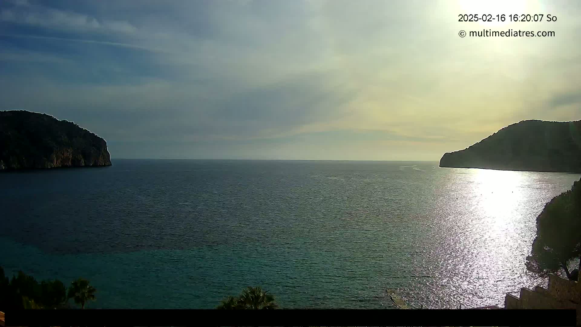 A calm sea with two dark, rocky headlands on either side, under a partly cloudy sky.