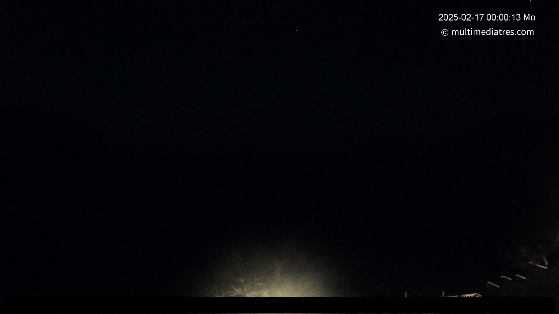 A nighttime outdoor scene shows a dark sky with a faint light source near the bottom, possibly from a low-lying light or the glow of a nearby town.