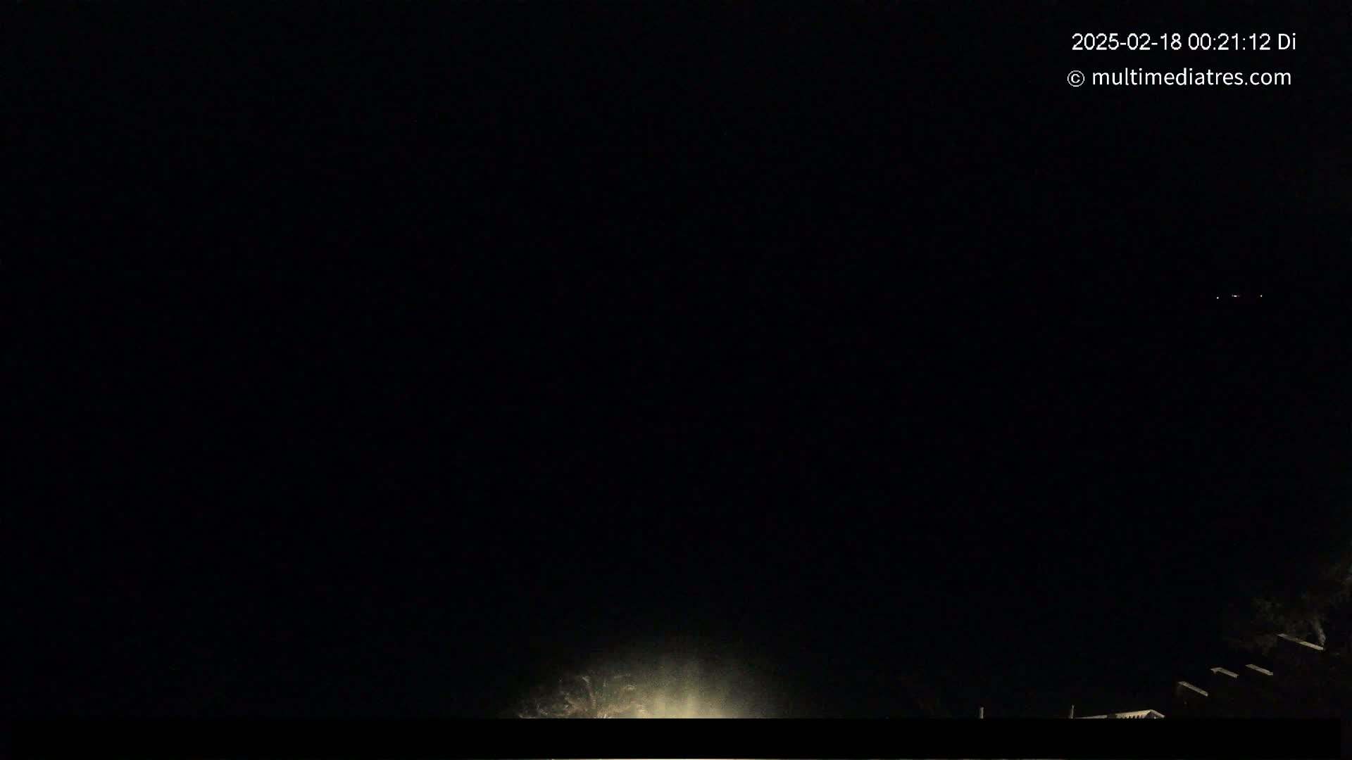 A nighttime, dark image shows a faint light source at the bottom and a few distant lights in the upper right corner.