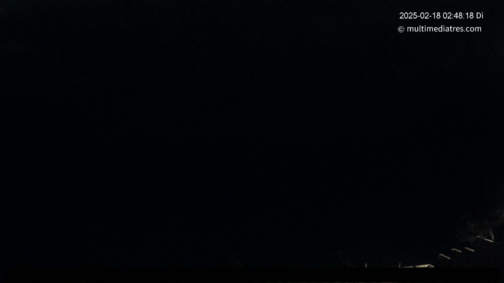 A nighttime outdoor scene shows a very dark sky and the faint silhouettes of structures at the bottom of the frame.
