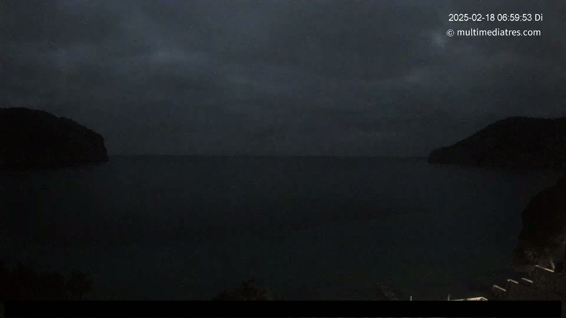 A dark, overcast night scene shows a body of water between two silhouetted hills.