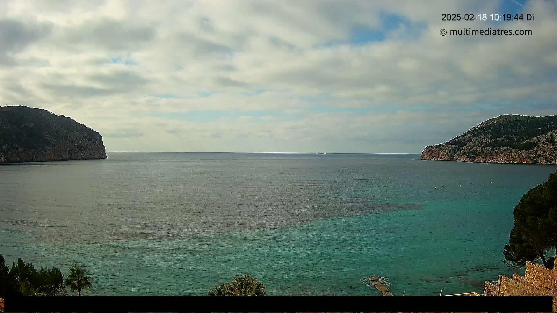 A partly cloudy day shows a calm body of teal and gray-green water nestled between two rocky cliffs.
