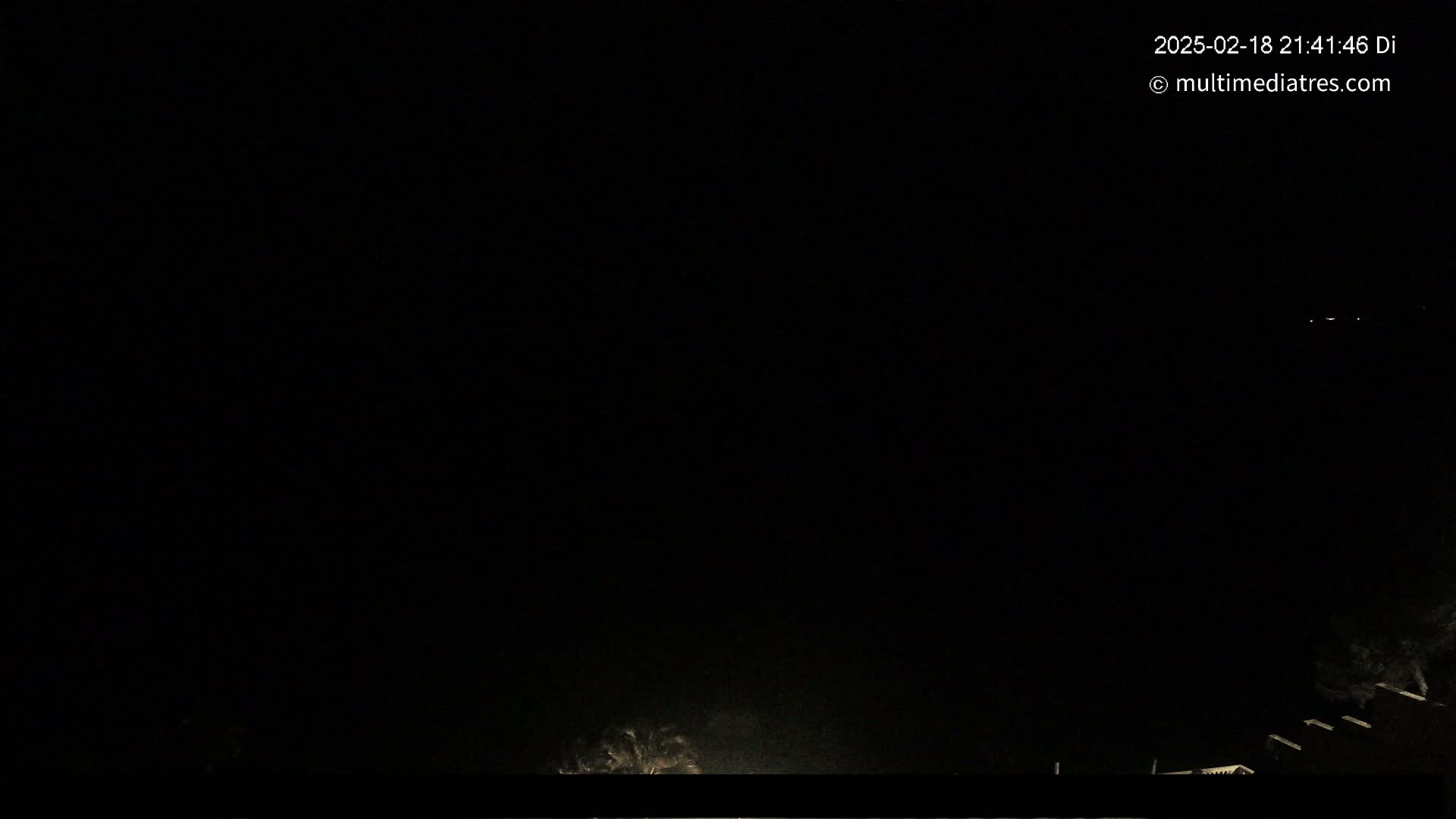 A nighttime, dark outdoor scene shows a few distant lights and a dark silhouette of a structure at the bottom of the frame.