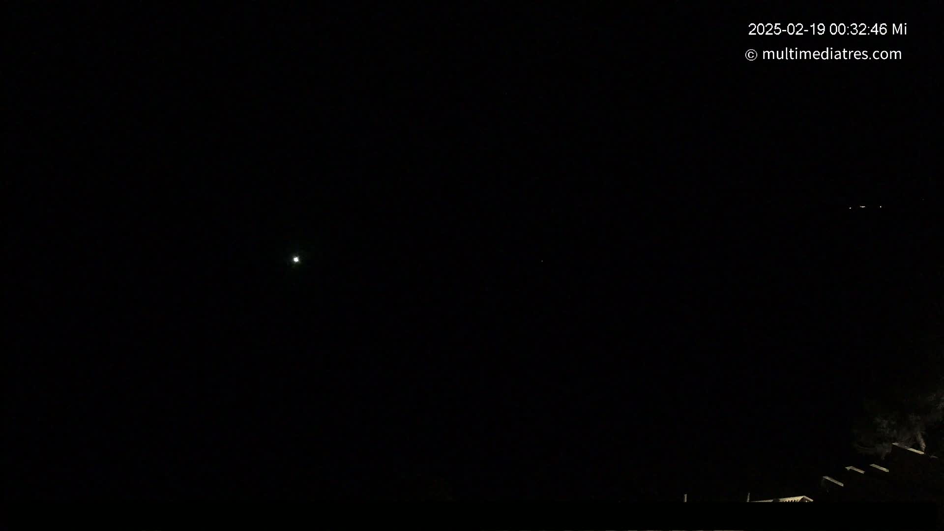 A dark, nighttime scene shows a few faint lights in the distance against a black sky.