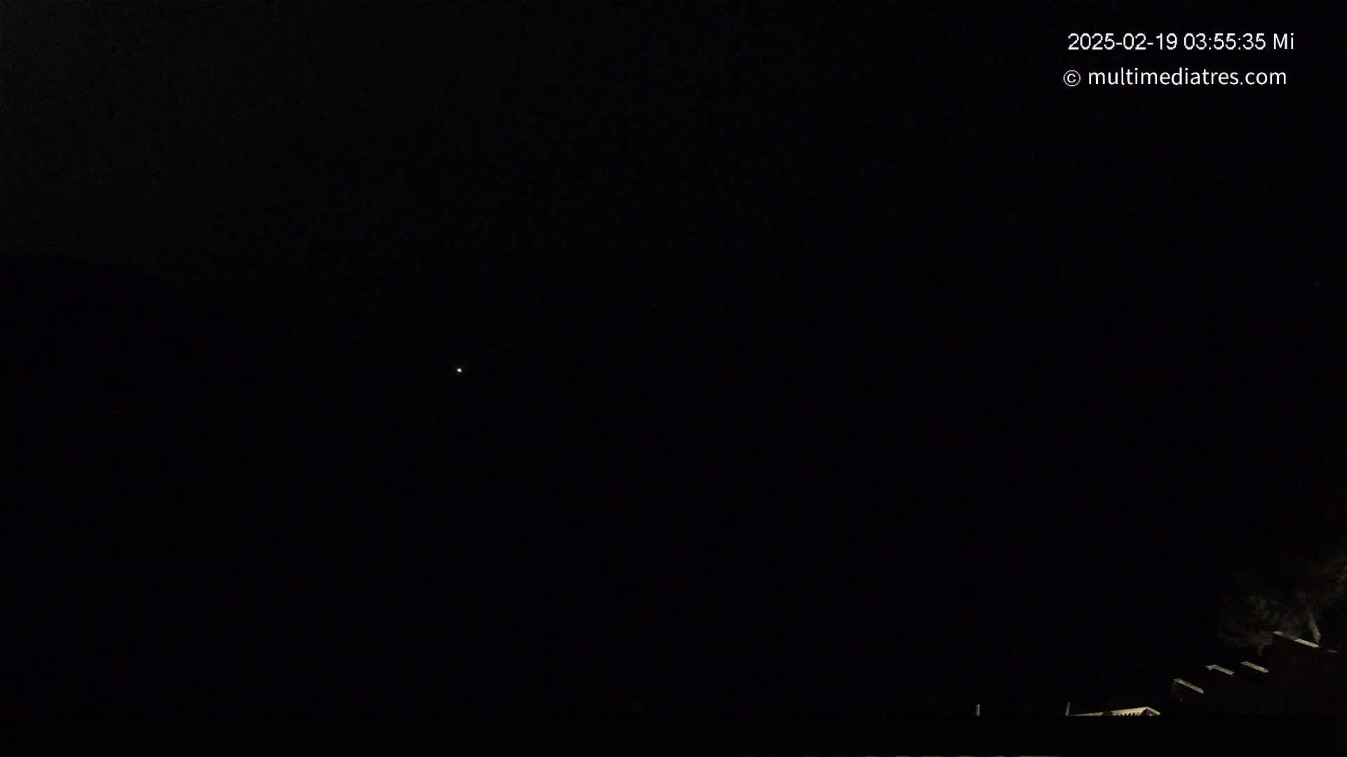 A single, faint light is visible in a dark night sky, with the silhouettes of structures barely visible in the lower right corner.