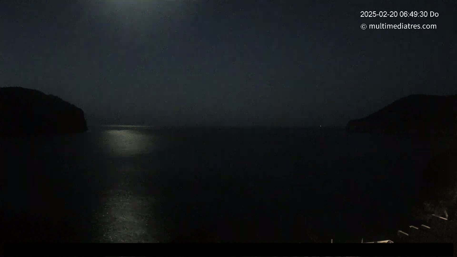 A moonlit night scene shows a dark body of water between two silhouetted hills.