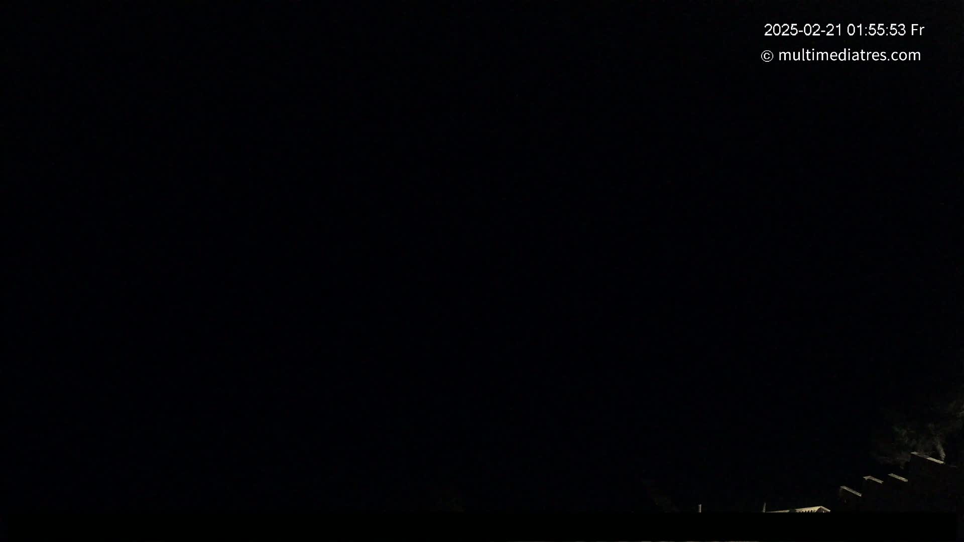 A nighttime, outdoor scene shows a mostly dark sky with a few dimly lit structures visible at the bottom.