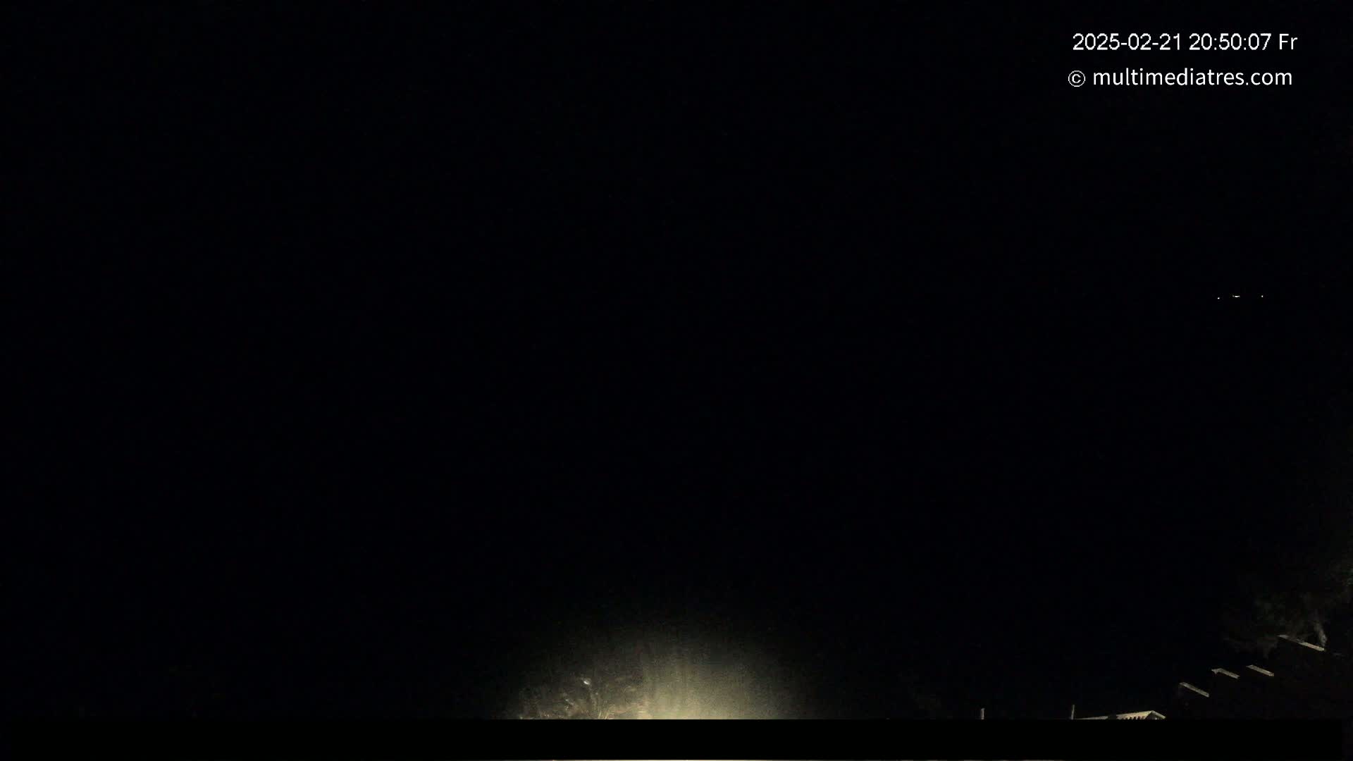 A nighttime view shows a dark sky with a few faint lights in the distance and a bright light source at the bottom center.