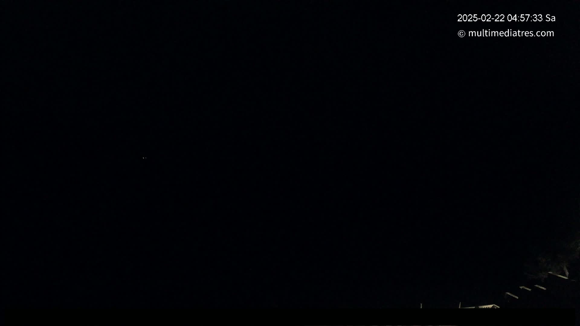 A dark nighttime scene shows a few faint lights in the distance and a suggestion of structures at the very bottom of the frame.