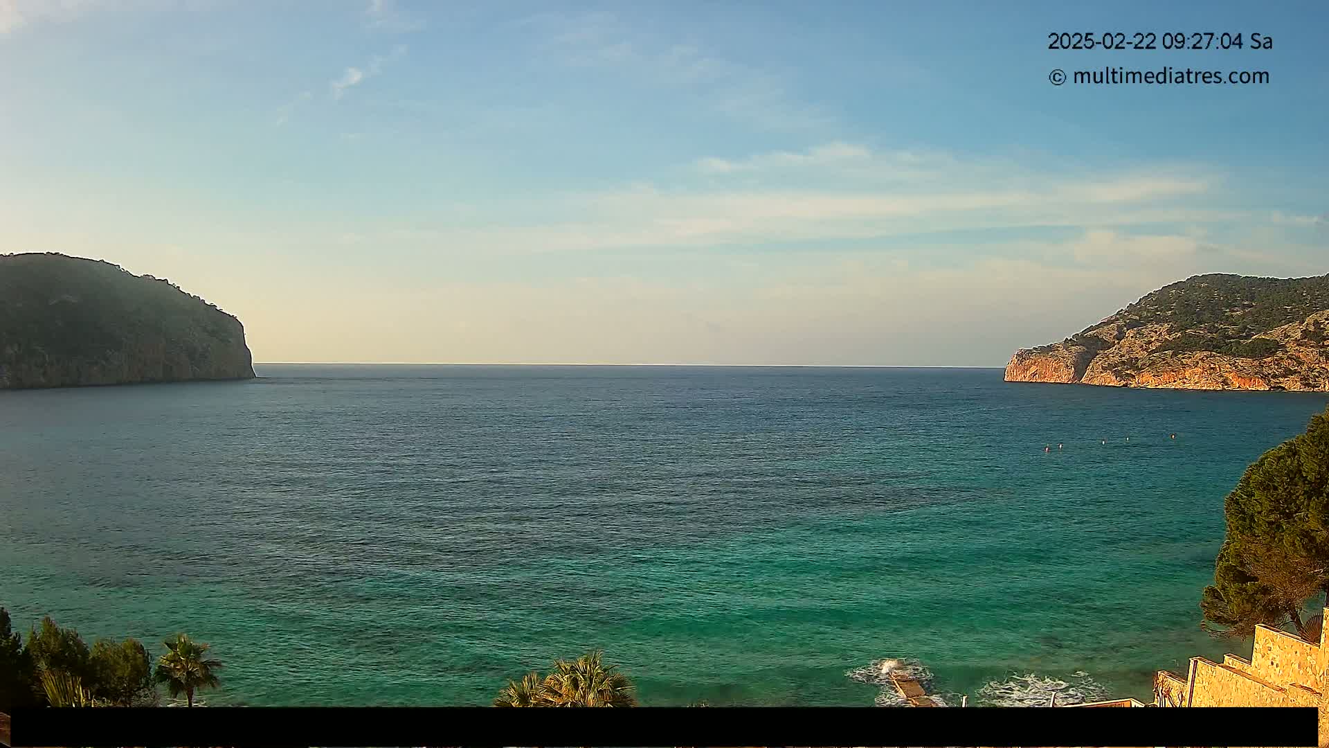 A calm, clear day shows a turquoise sea nestled between two rocky hills.
