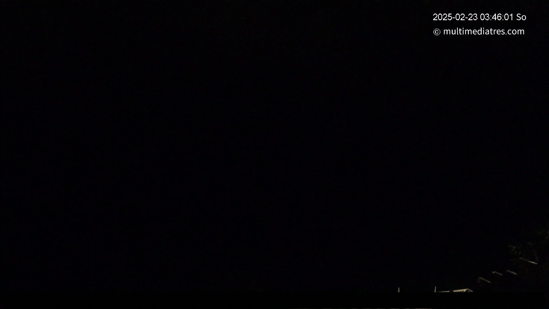 The image shows a completely dark night scene with a few dimly lit structures visible at the very bottom.