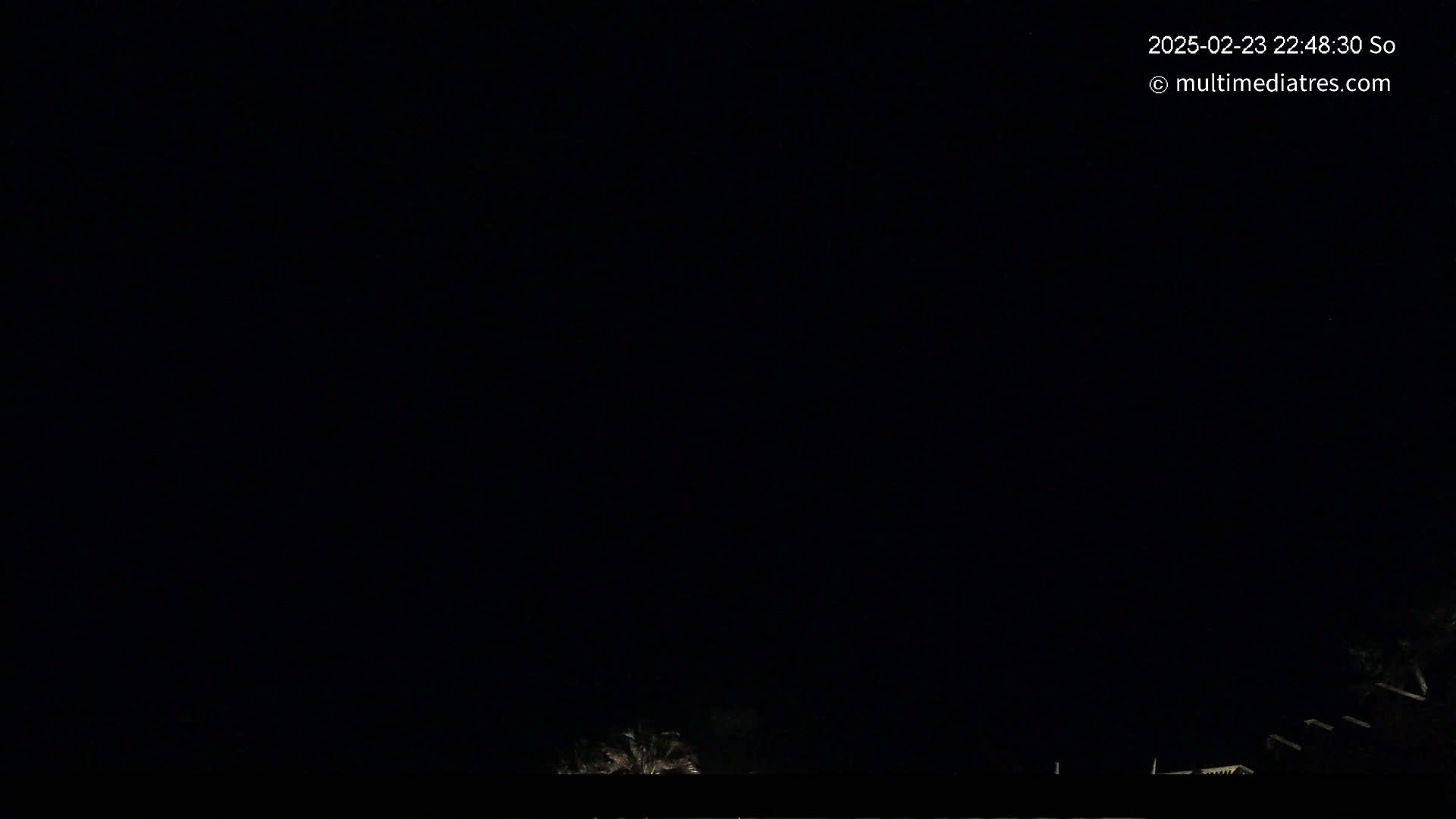 A nighttime outdoor scene shows a dark sky with faintly visible silhouettes of trees and structures at the bottom.