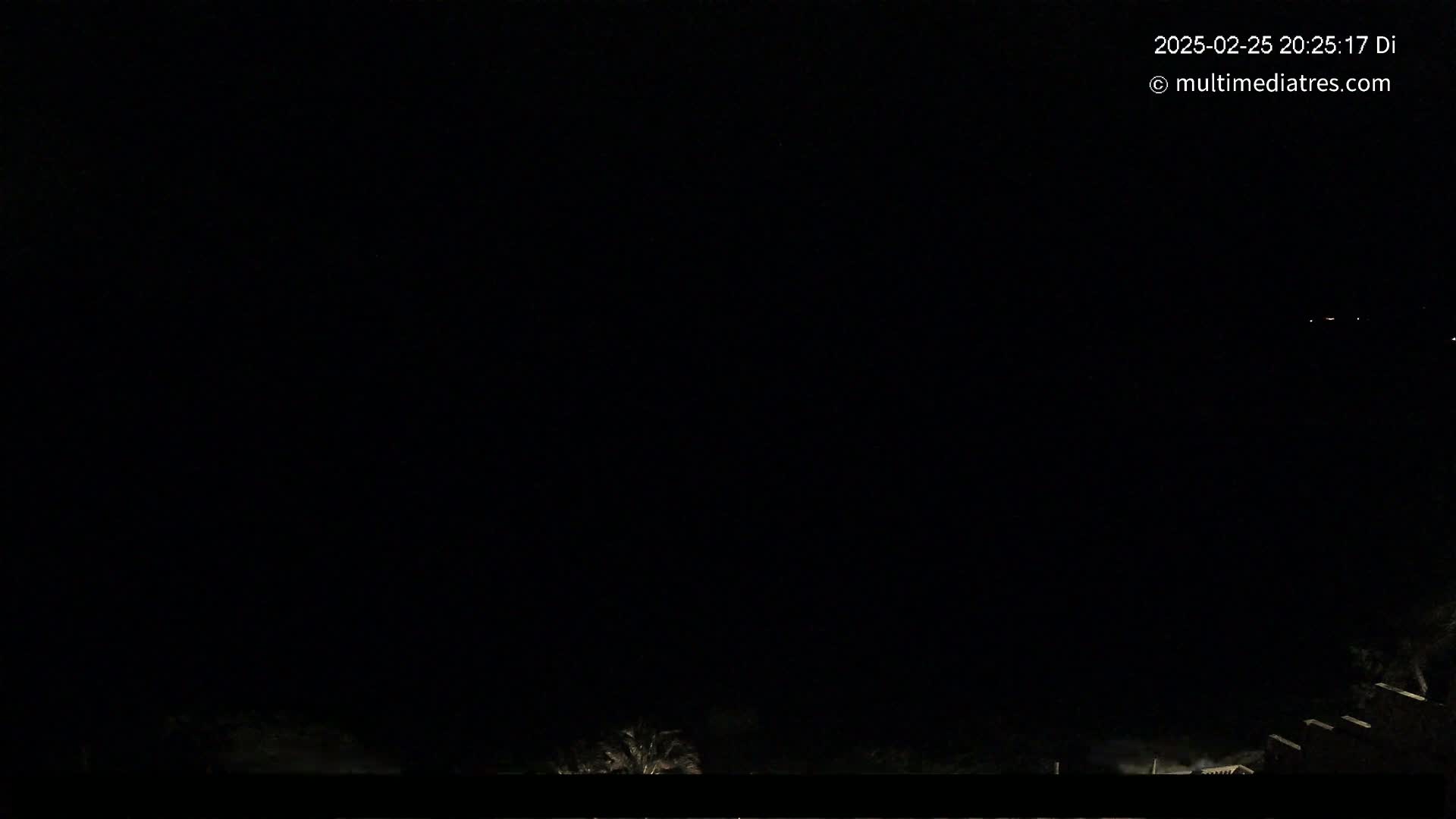 A nighttime, dark scene shows a few distant lights against a mostly black sky, with some vegetation visible at the bottom.
