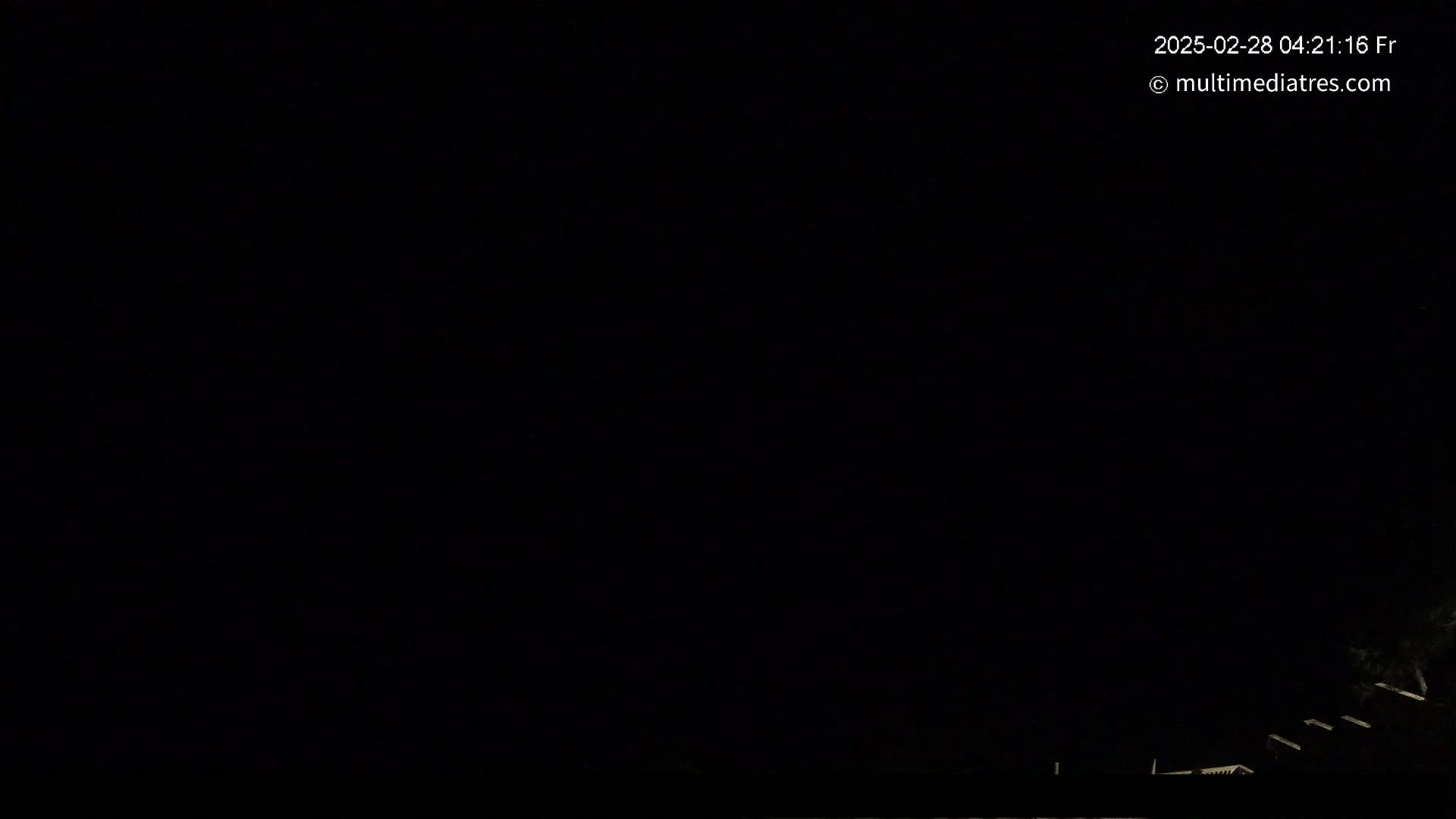 The image shows a very dark night scene with only a few dimly lit structures visible at the very bottom.