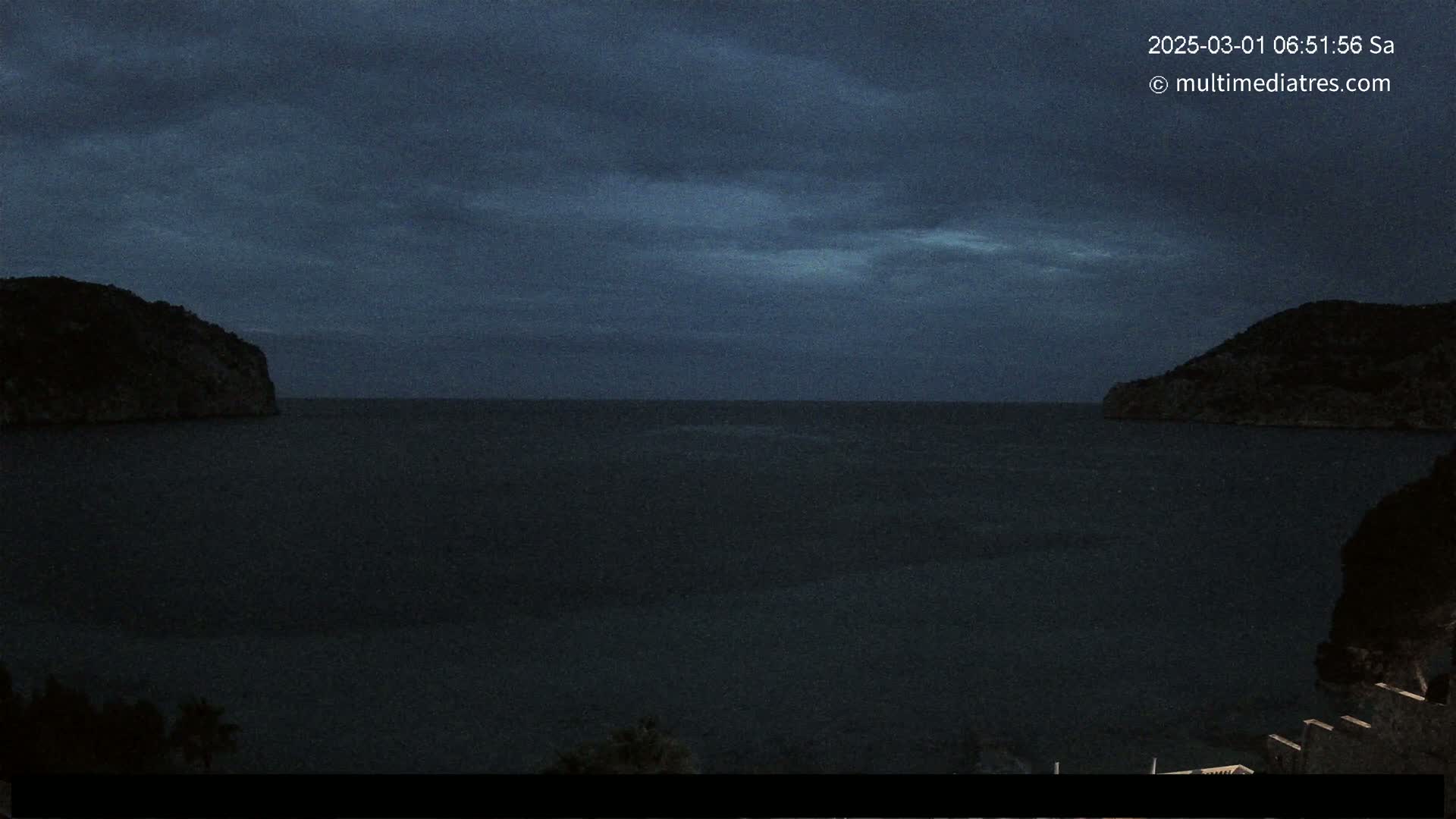 A dark, calm body of water is nestled between two silhouetted hills under a cloudy, twilight sky.