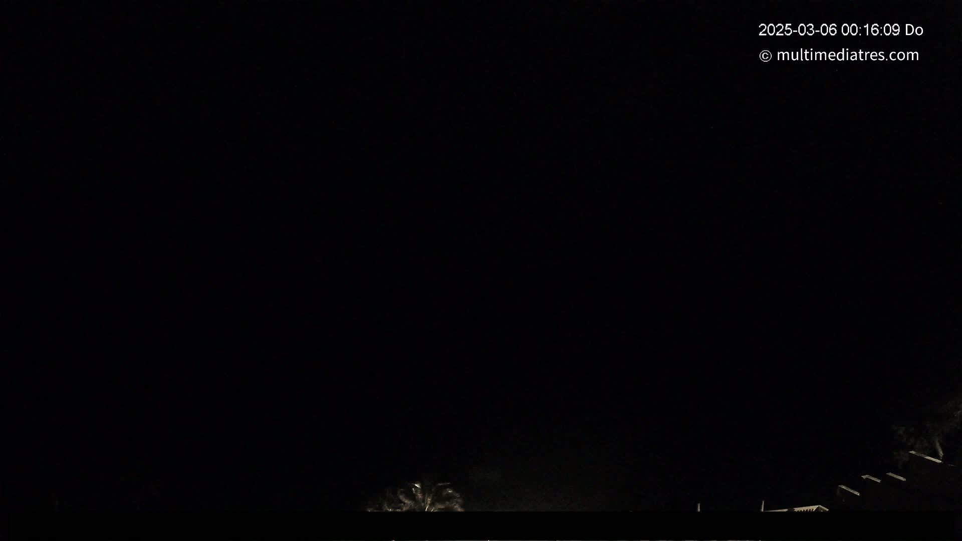 The image shows a nighttime outdoor scene with a dark sky and faintly visible silhouettes of trees and structures at the bottom.